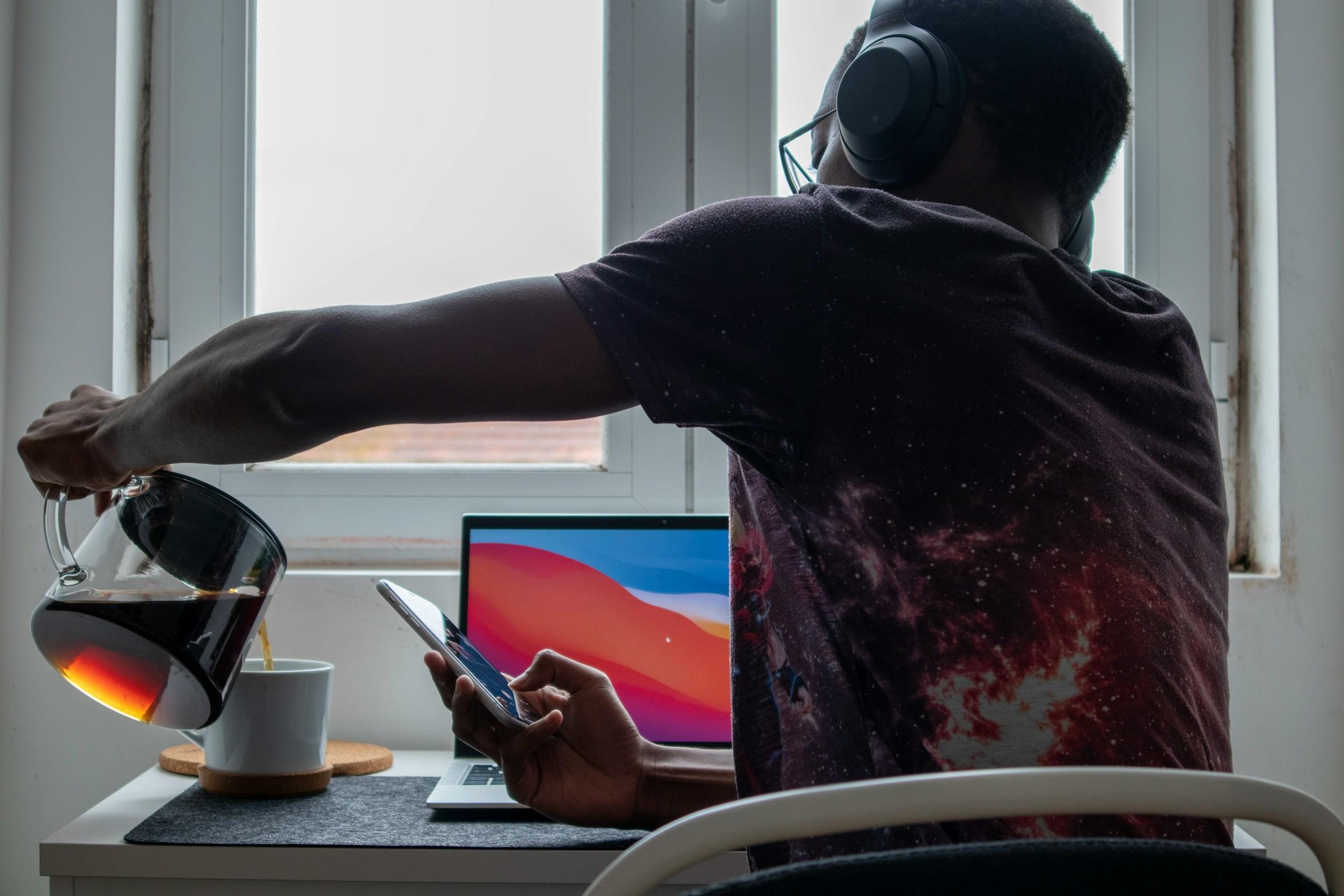Persoon met koptelefoon op en IPhone in hand schenkt koffie in