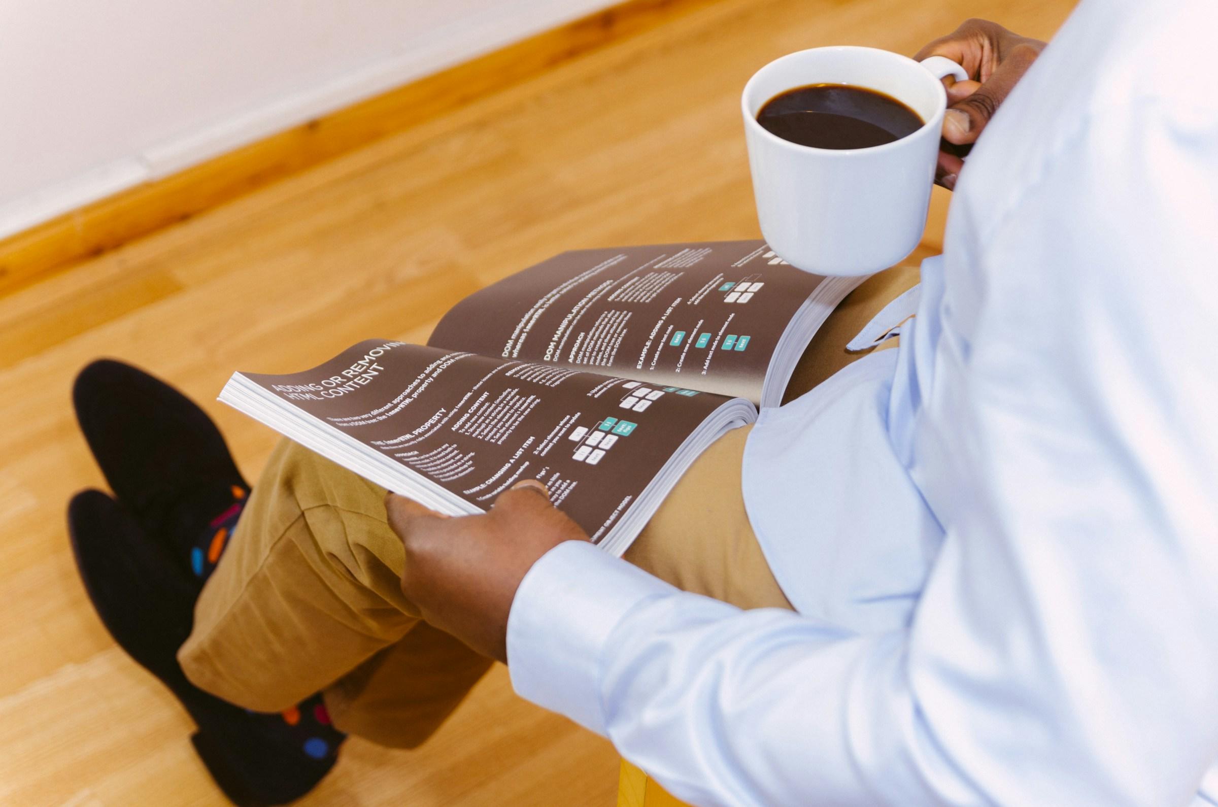 Zittende persoon met koffie in de hand en tijdschrift op schoot