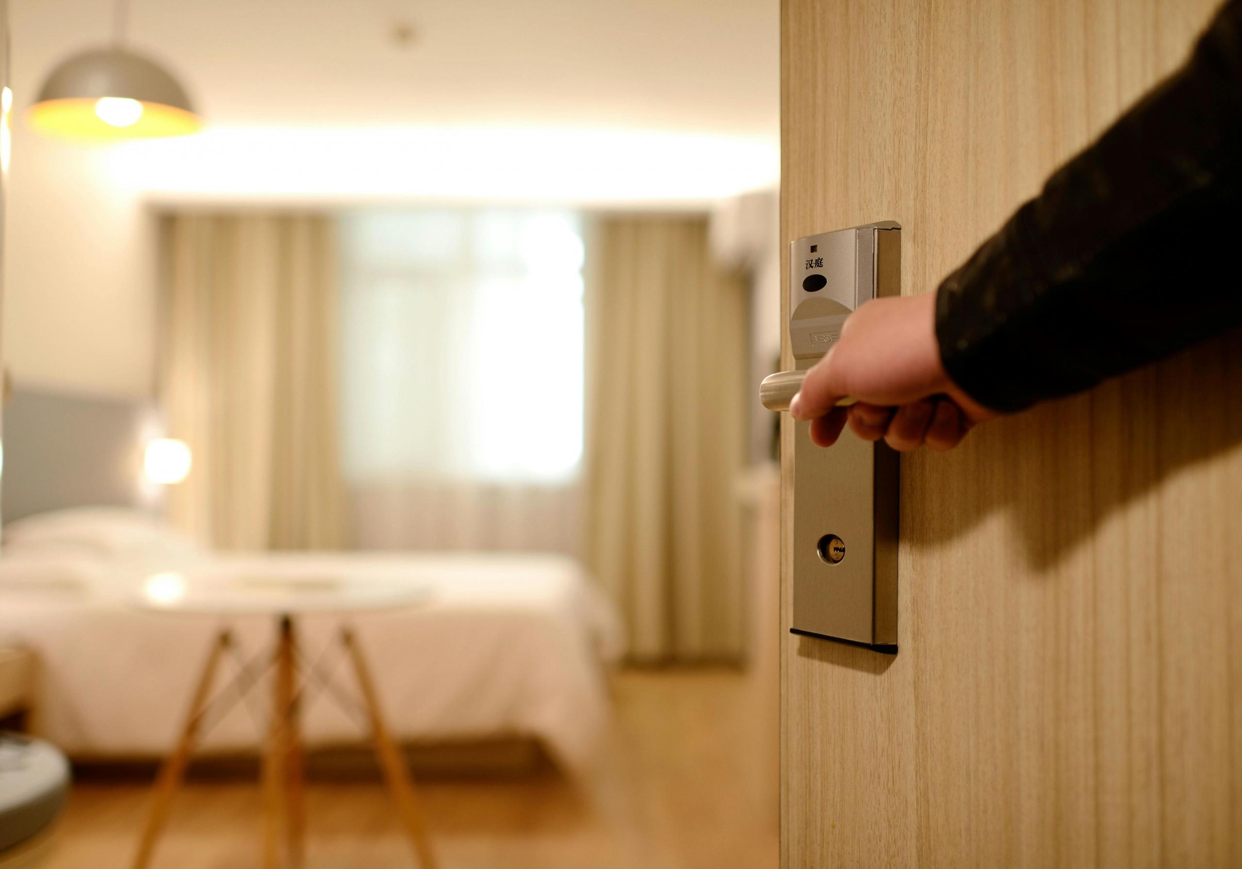 Een persoon opent een deur naar een moderne hotelkamer.