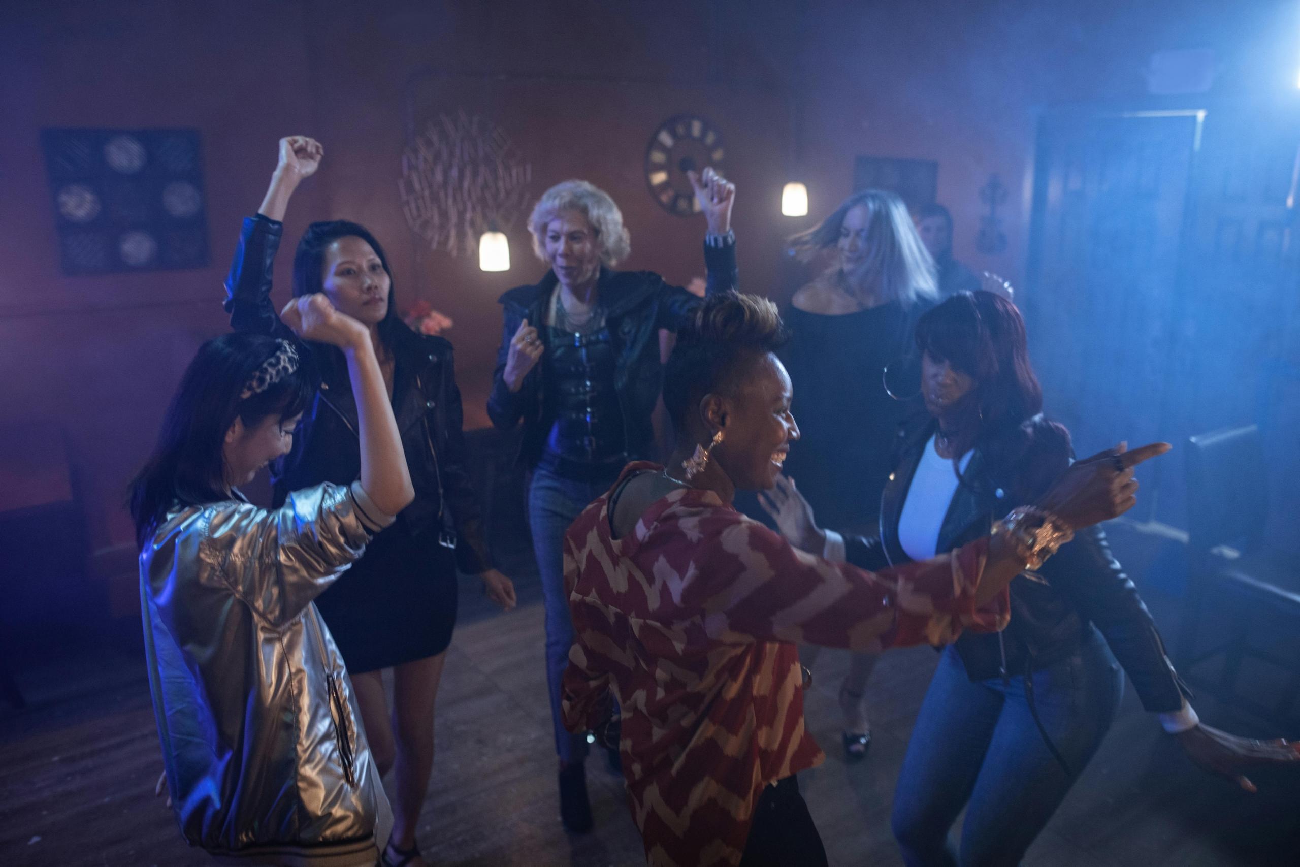 Mensen dansen en vieren feest in een barachtige omgeving met donkere verlichting en een dansvloer.