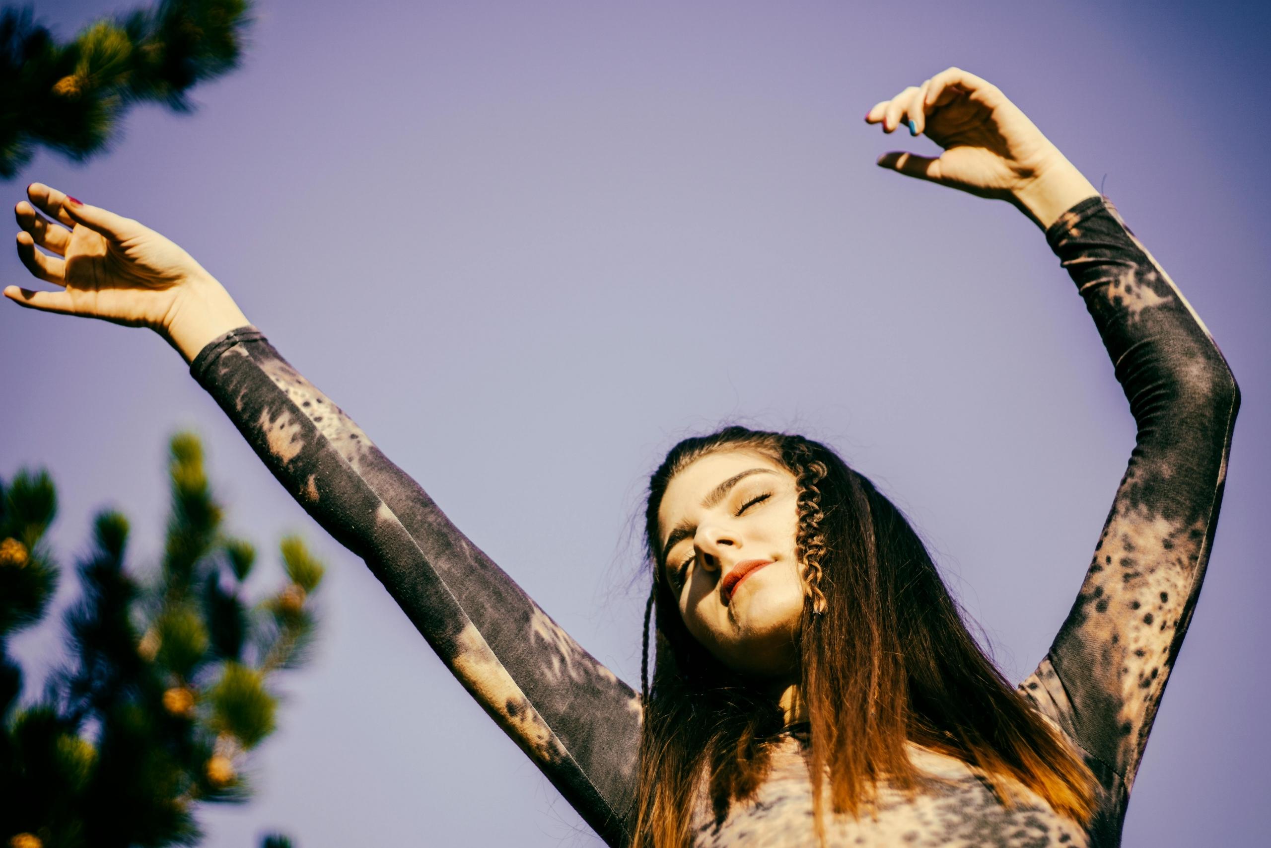 Een vrouw danst buiten met haar armen geheven tegen een blauwe lucht.