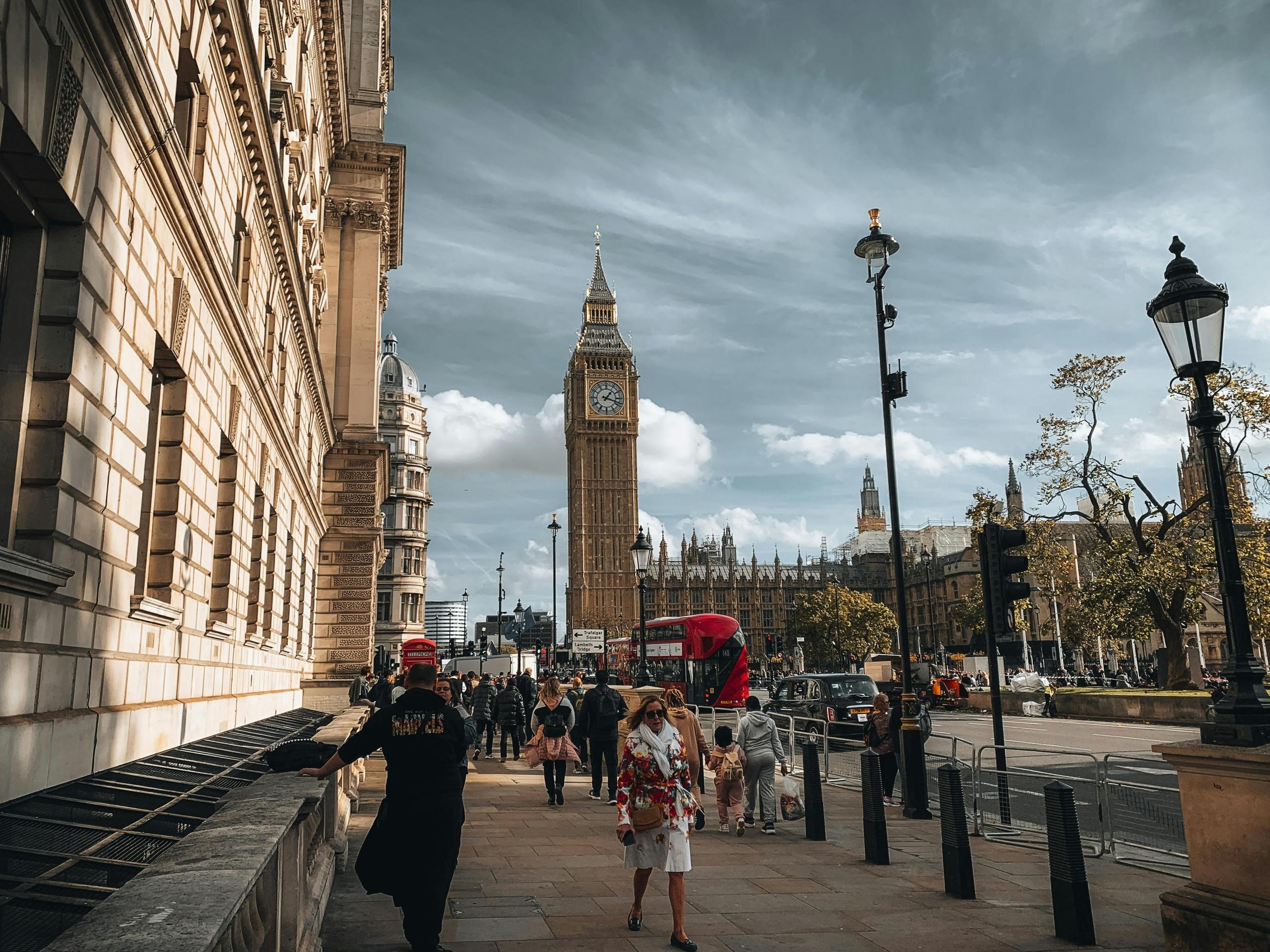Een levendige straatscène nabij de Big Ben in Londen, met mensen die wandelen en traditionele elementen zoals rode bussen en zwarte taxi's.