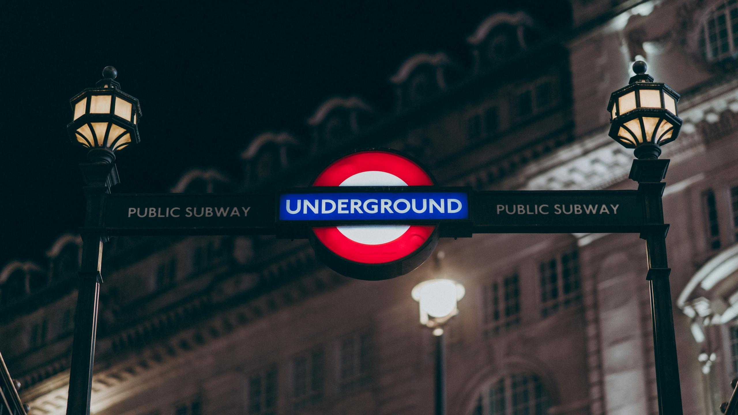 Een nachtelijk beeld van een London Underground bord met dramatische verlichting tegen een achtergrond van een historisch gebouw.