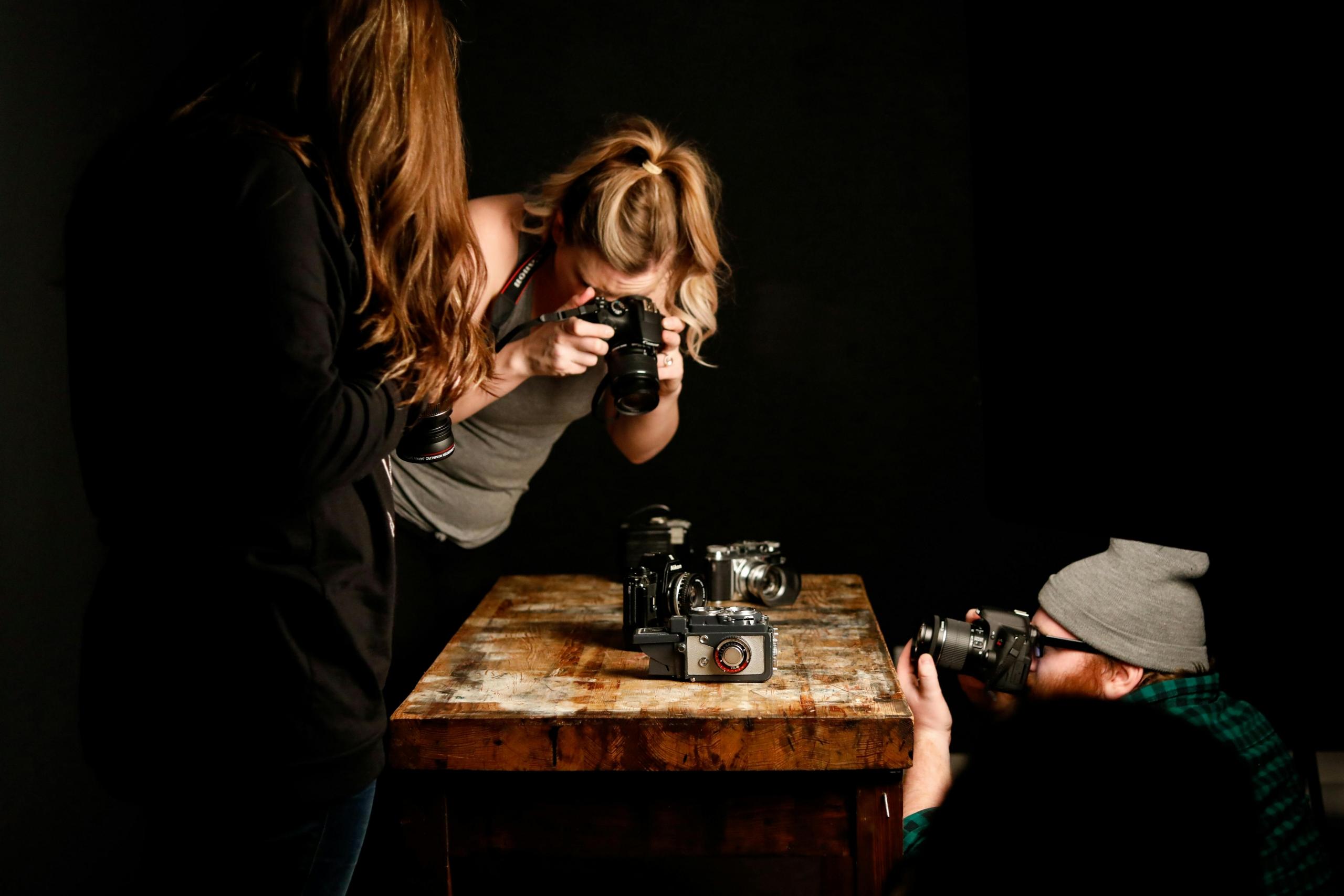 Twee vrouwen bestuderen een camera in een donkere studio, bezig met een fotosessie.