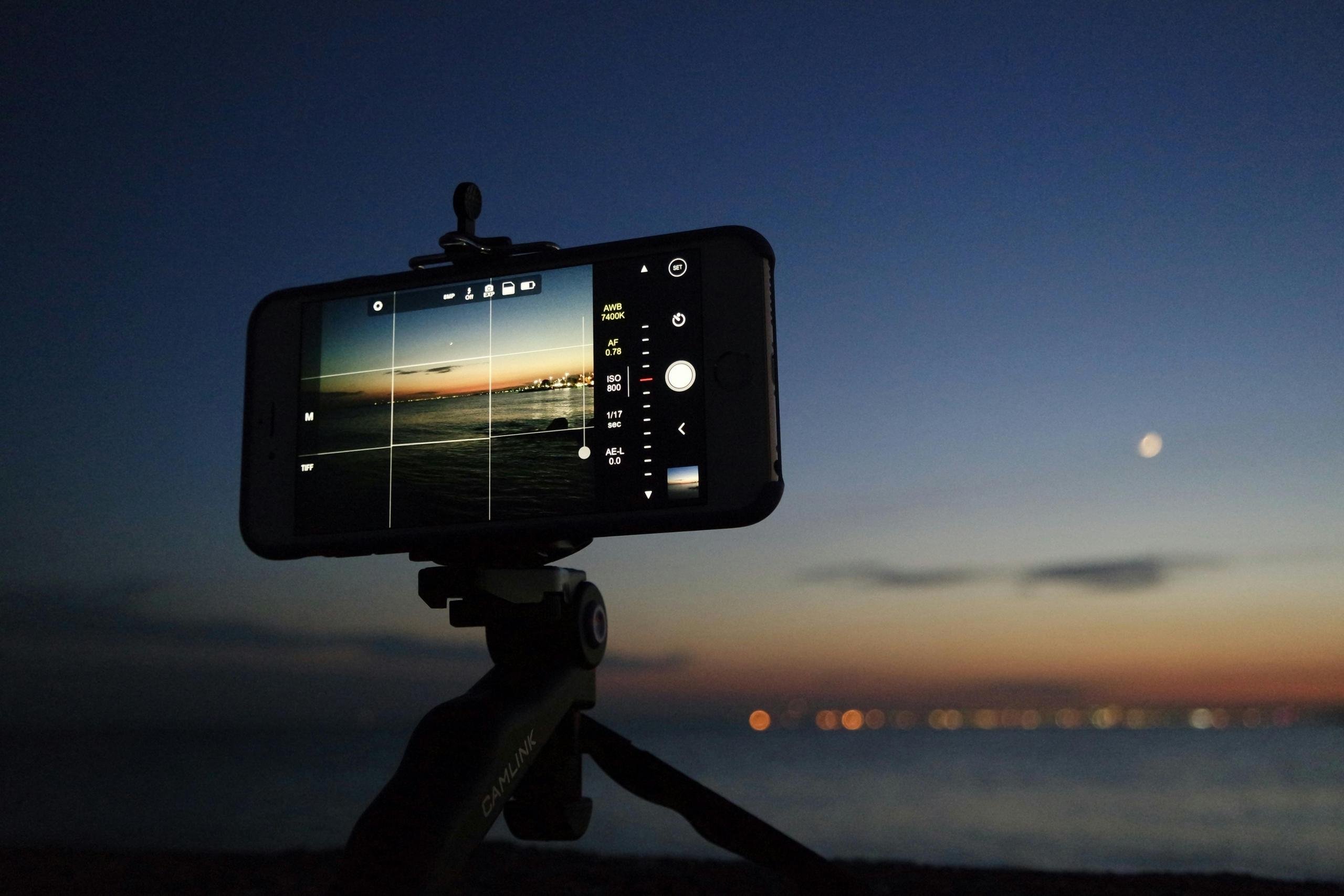 Een smartphone op een statief neemt een foto van een zonsondergang aan het strand.