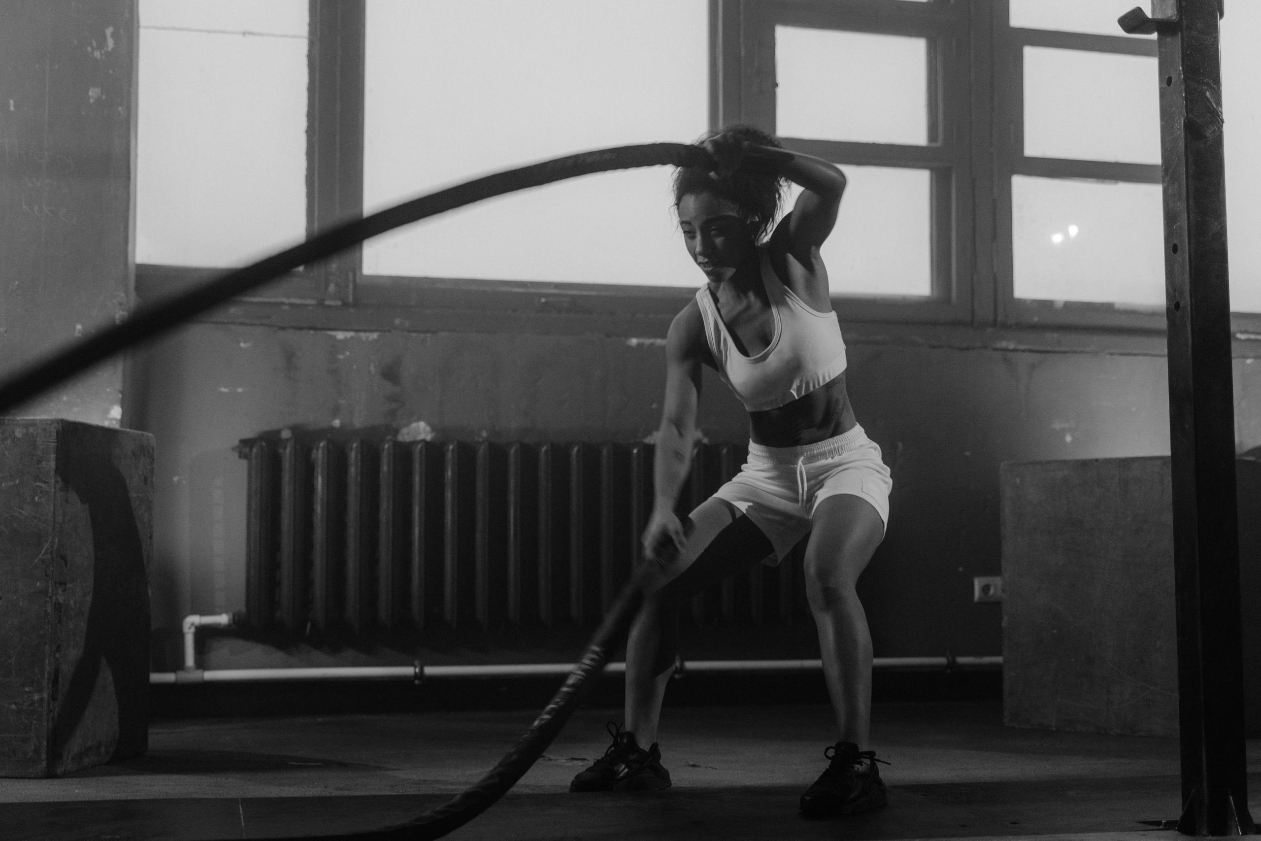 Een vrouw gebruikt een battle rope in een industriële sportschoolomgeving.