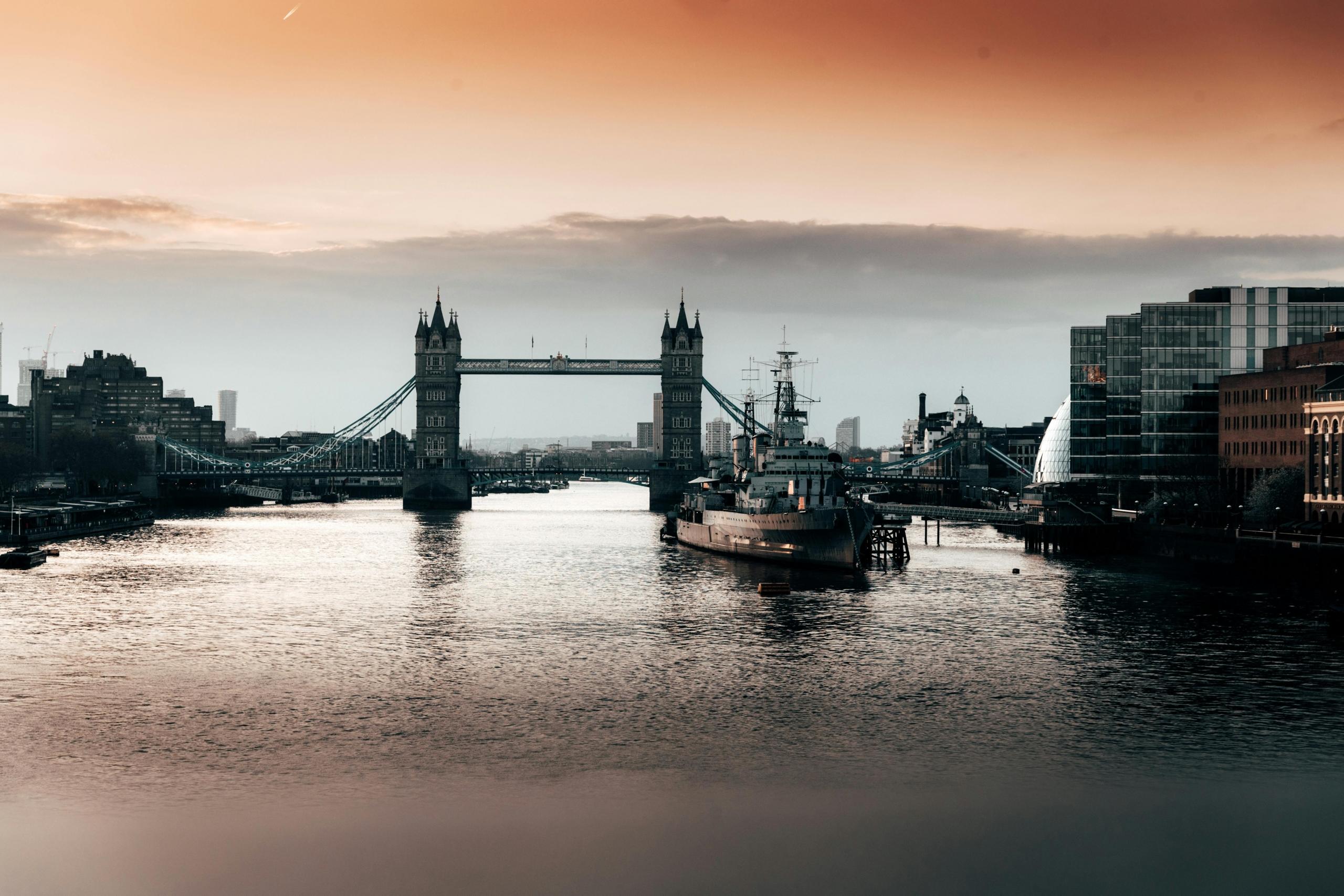 Een uitzicht op Tower Bridge en de rivier de Theems tijdens zonsondergang, met moderne gebouwen en een schip.