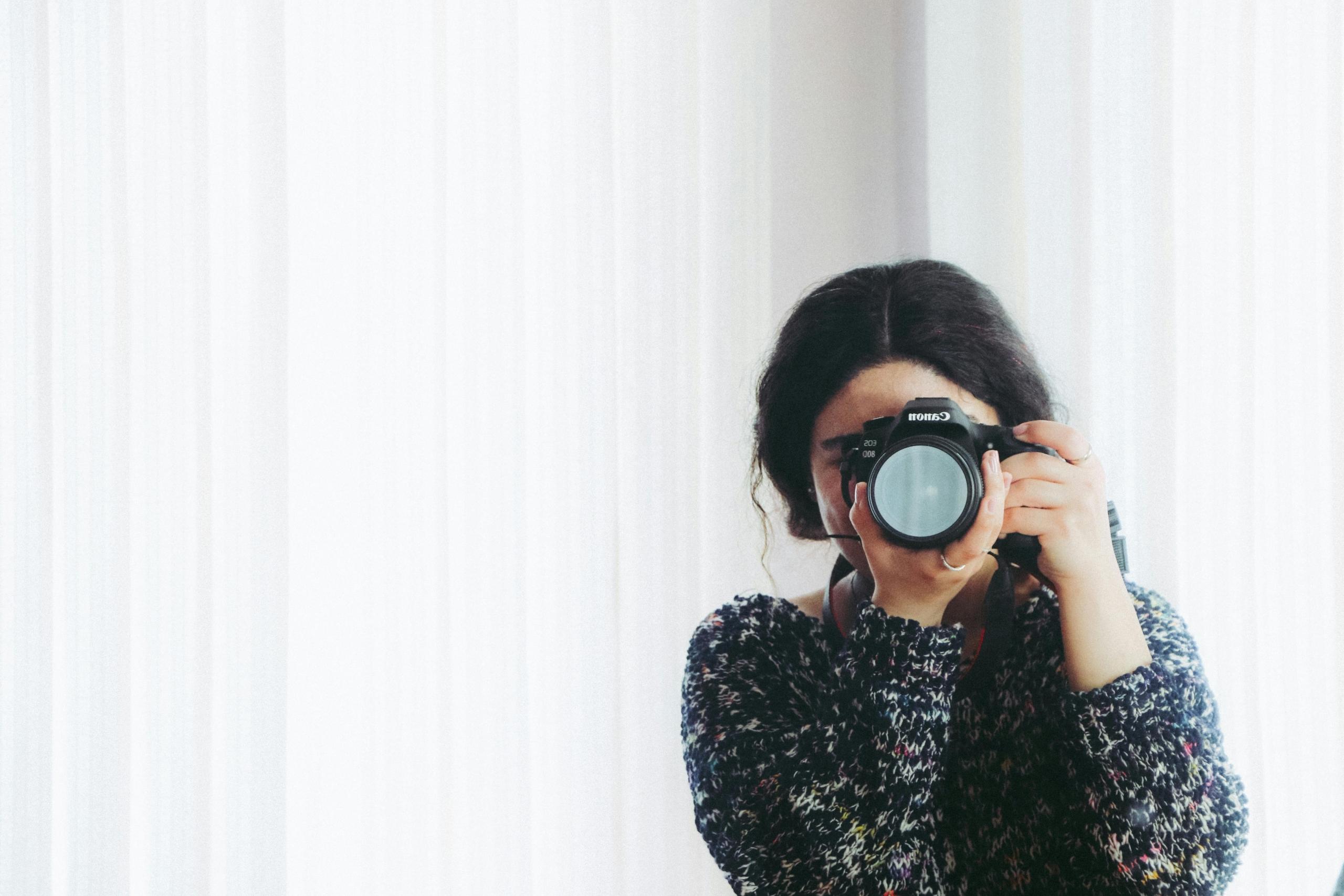 Een vrouwelijke fotograaf met een donkere trui fotografeert met een grote DSLR-camera.