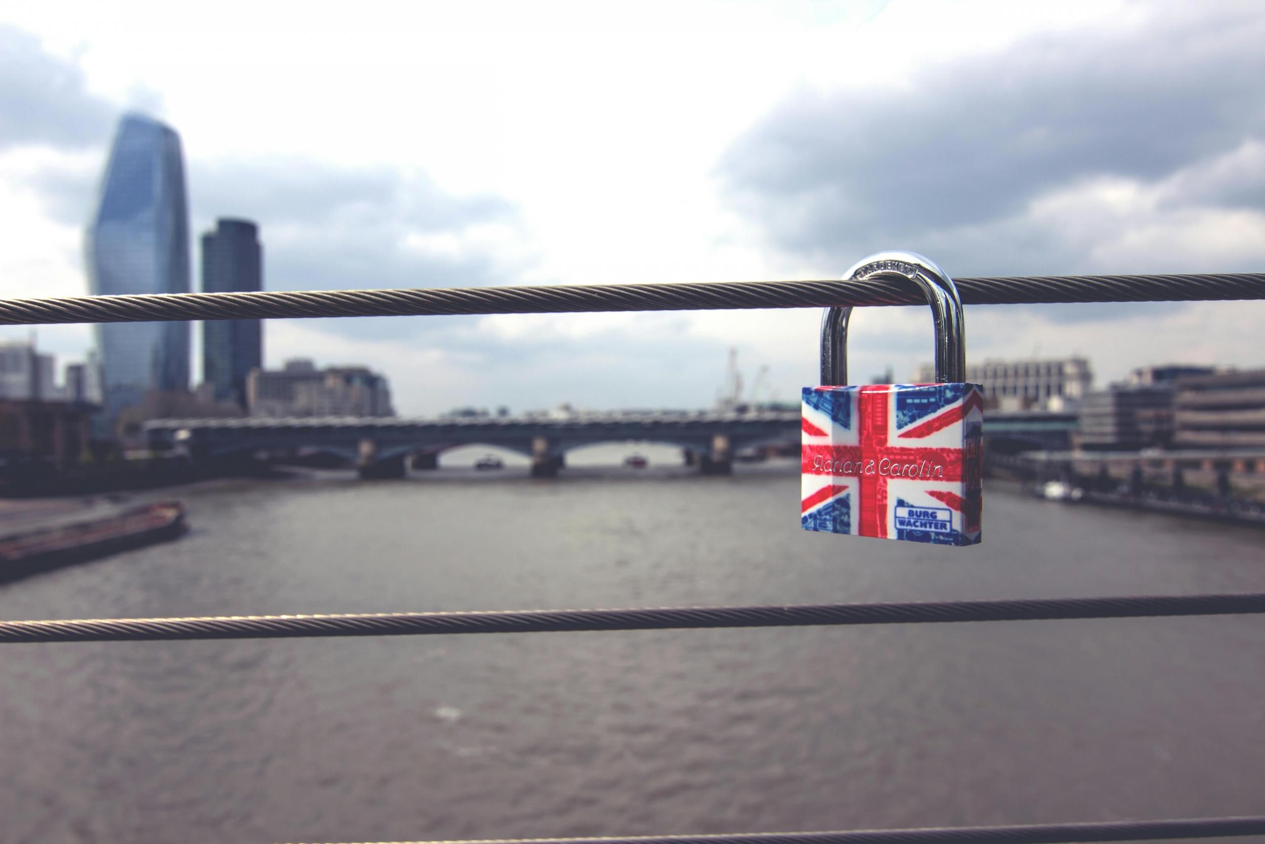 Een hangslot bedekt met een Britse vlag hangt aan een reling met de Theems en Londen op de achtergrond.
