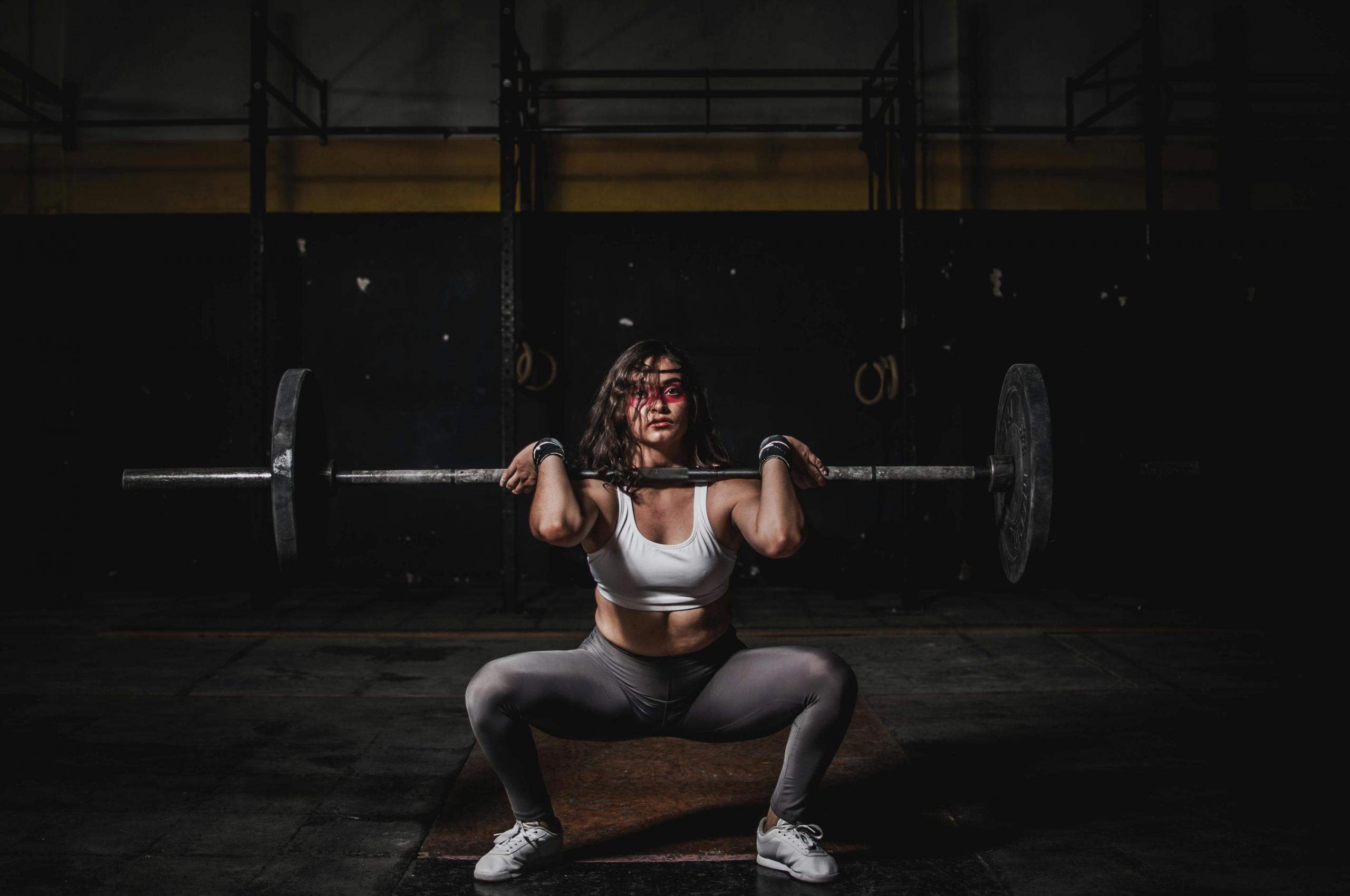 Een vrouw doet een squat met een halterstang in een donkere gym.