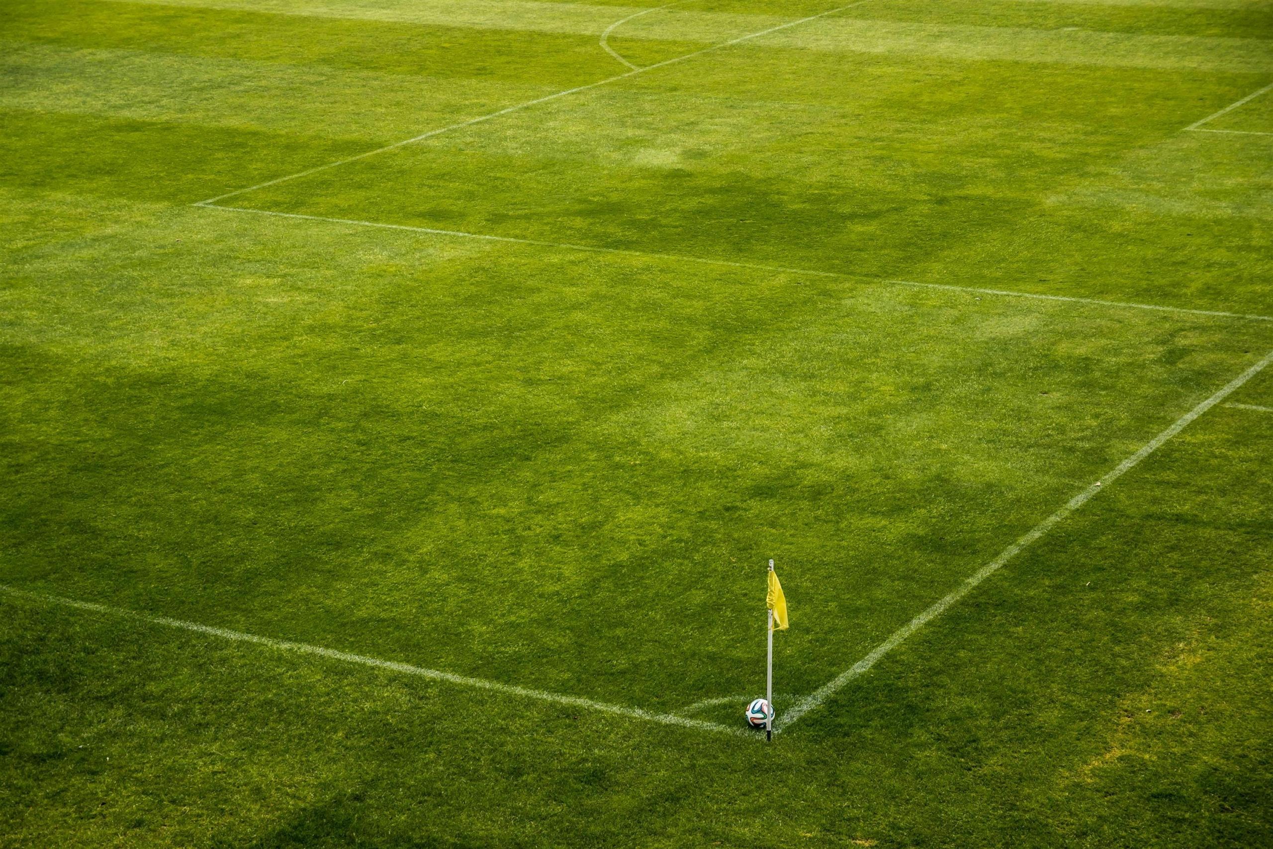 Een bovenaanzicht van een voetbalveld met een cornervlag en een voetbal.