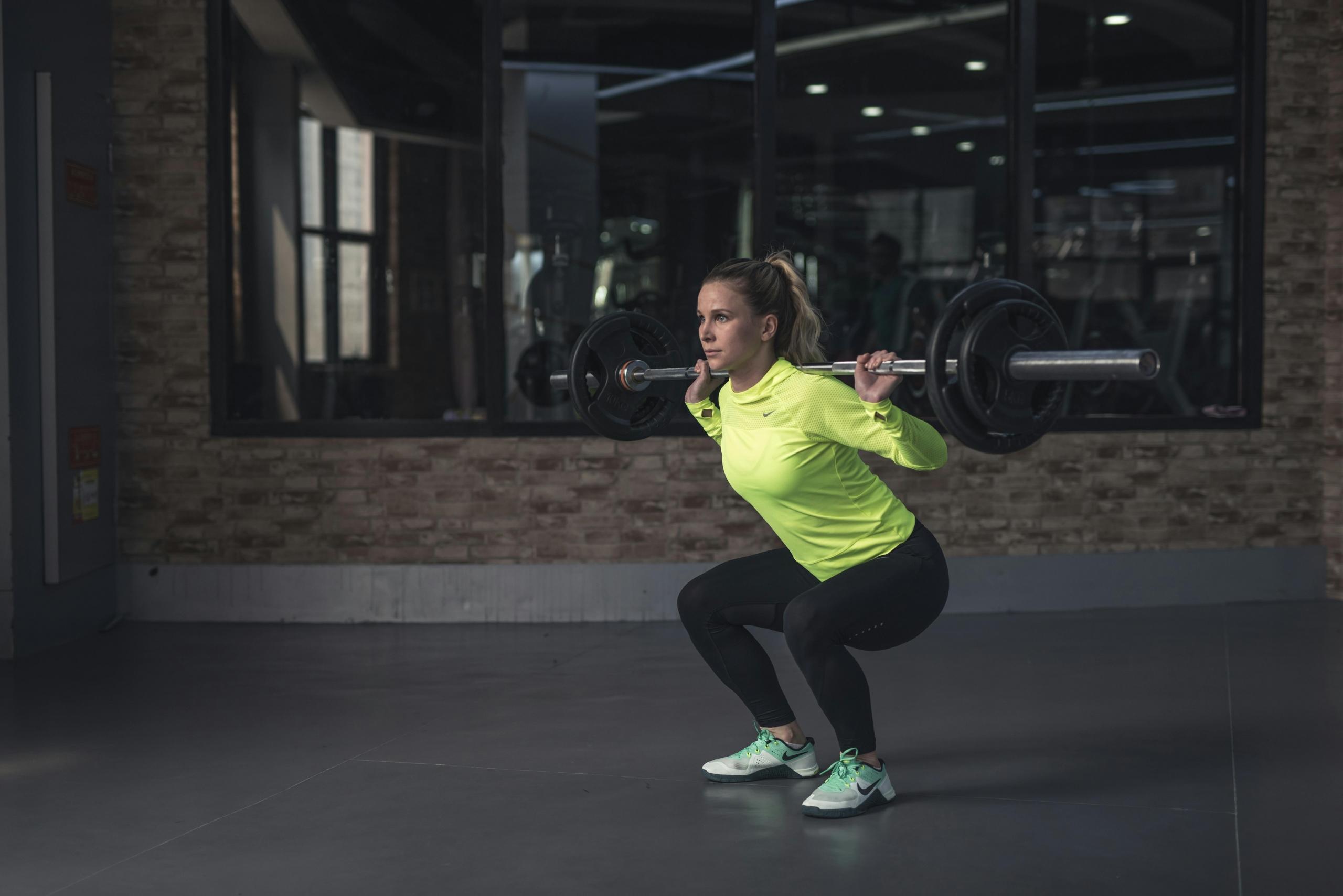 Een vrouw doet squats met een halterstang in een sportschool, gefocust op haar houding.