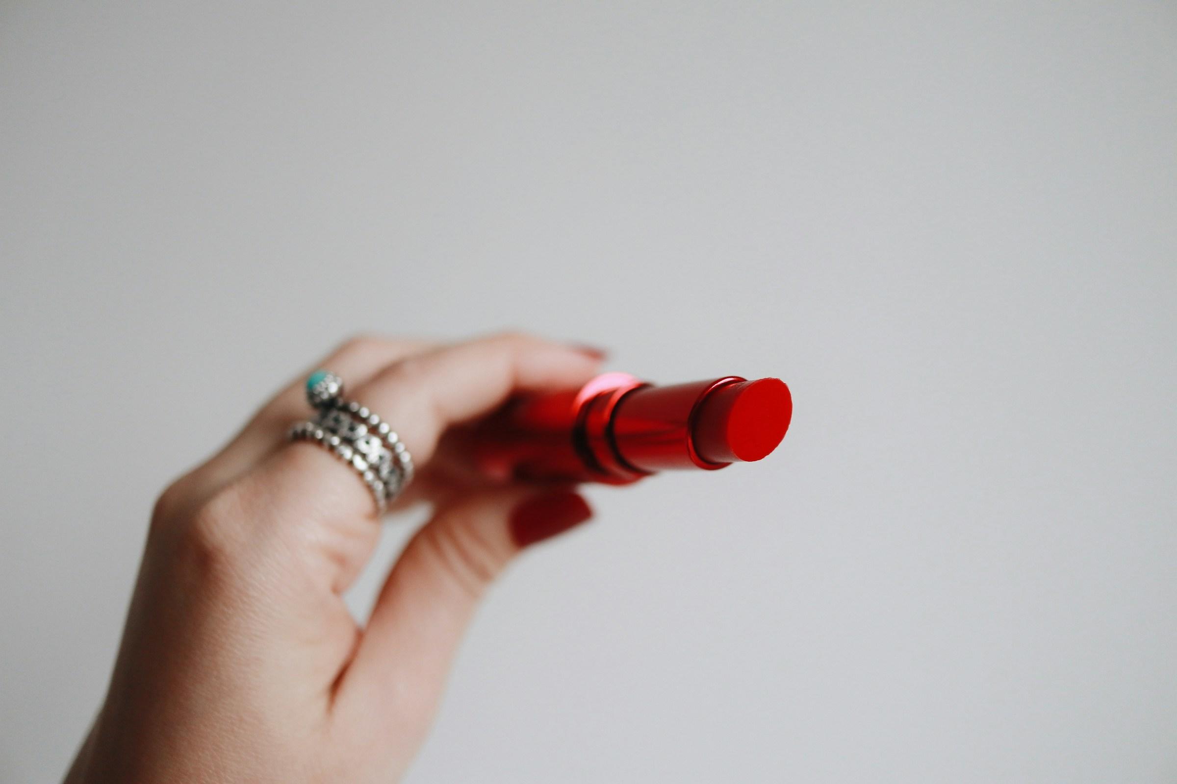 Hand met ring houdt rode lippenstift vast