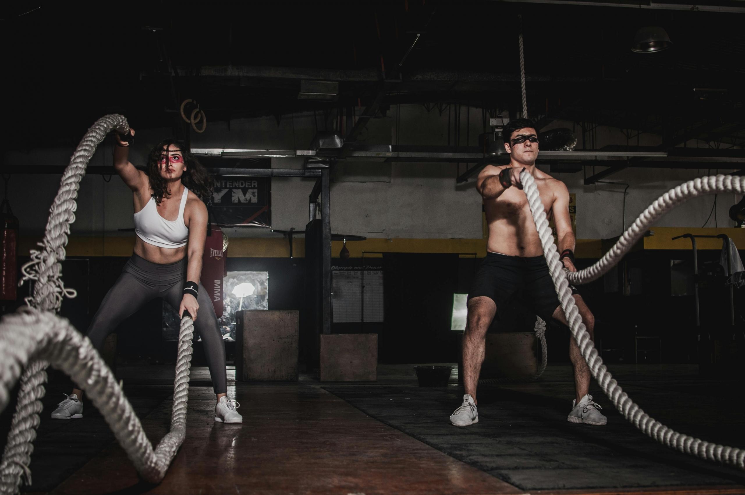 Een vrouw en een man die samen met battle ropes trainen in een donkere gym.