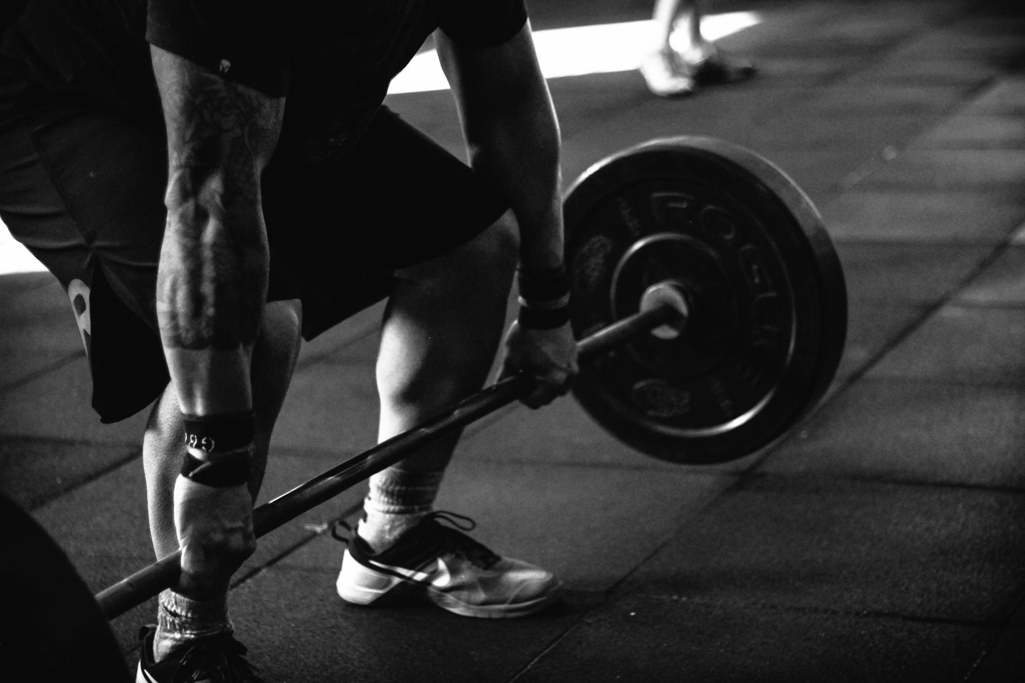 Een close-up van iemand die een deadlift doet met een zware halter in zwart-wit.