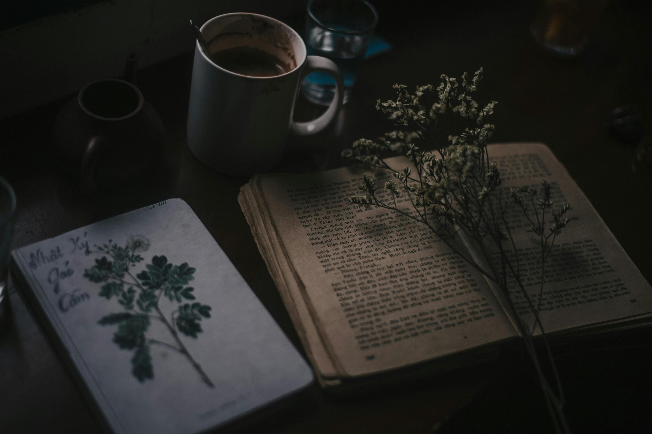 Een open oud boek ligt naast een kop koffie en bloemen in een donkere setting.