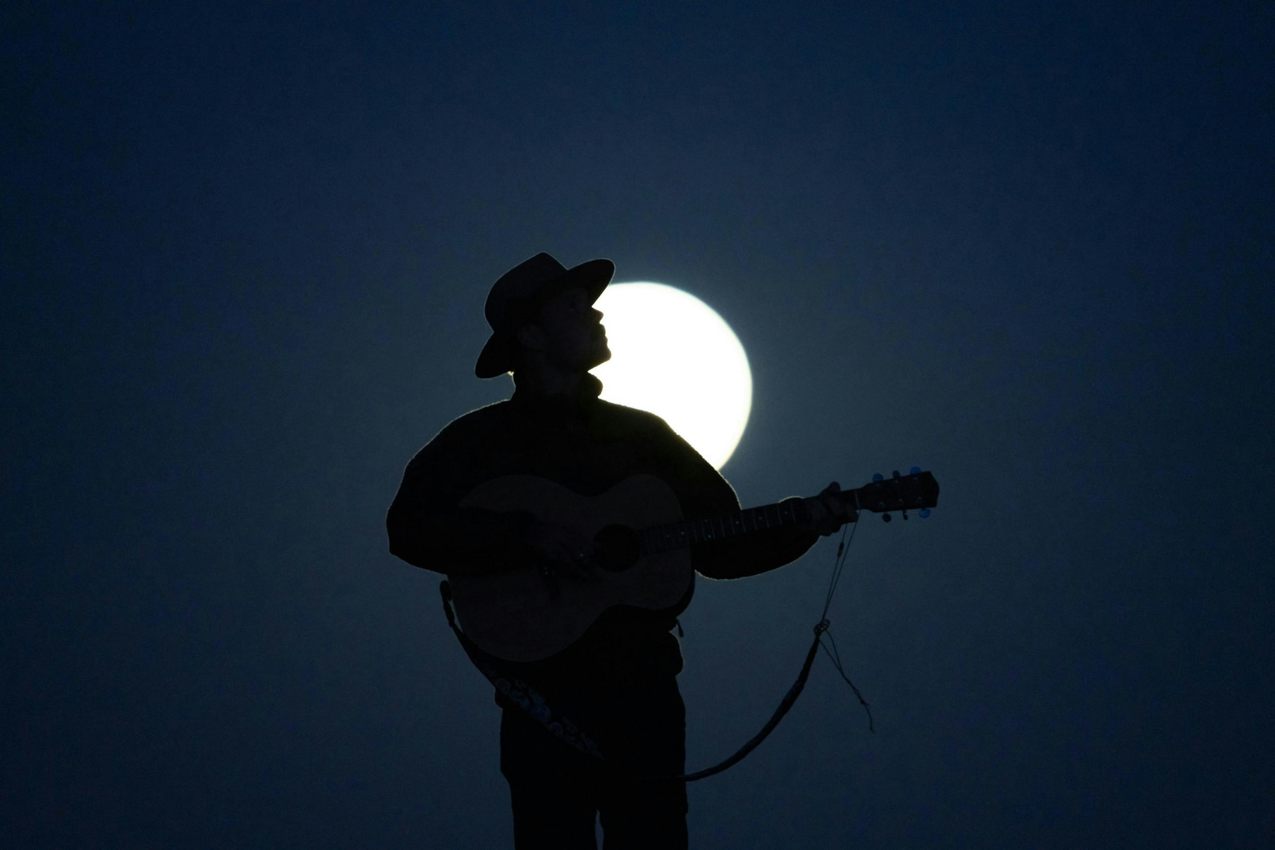 Een silhouet van een muzikant die gitaar speelt onder het licht van de volle maan.