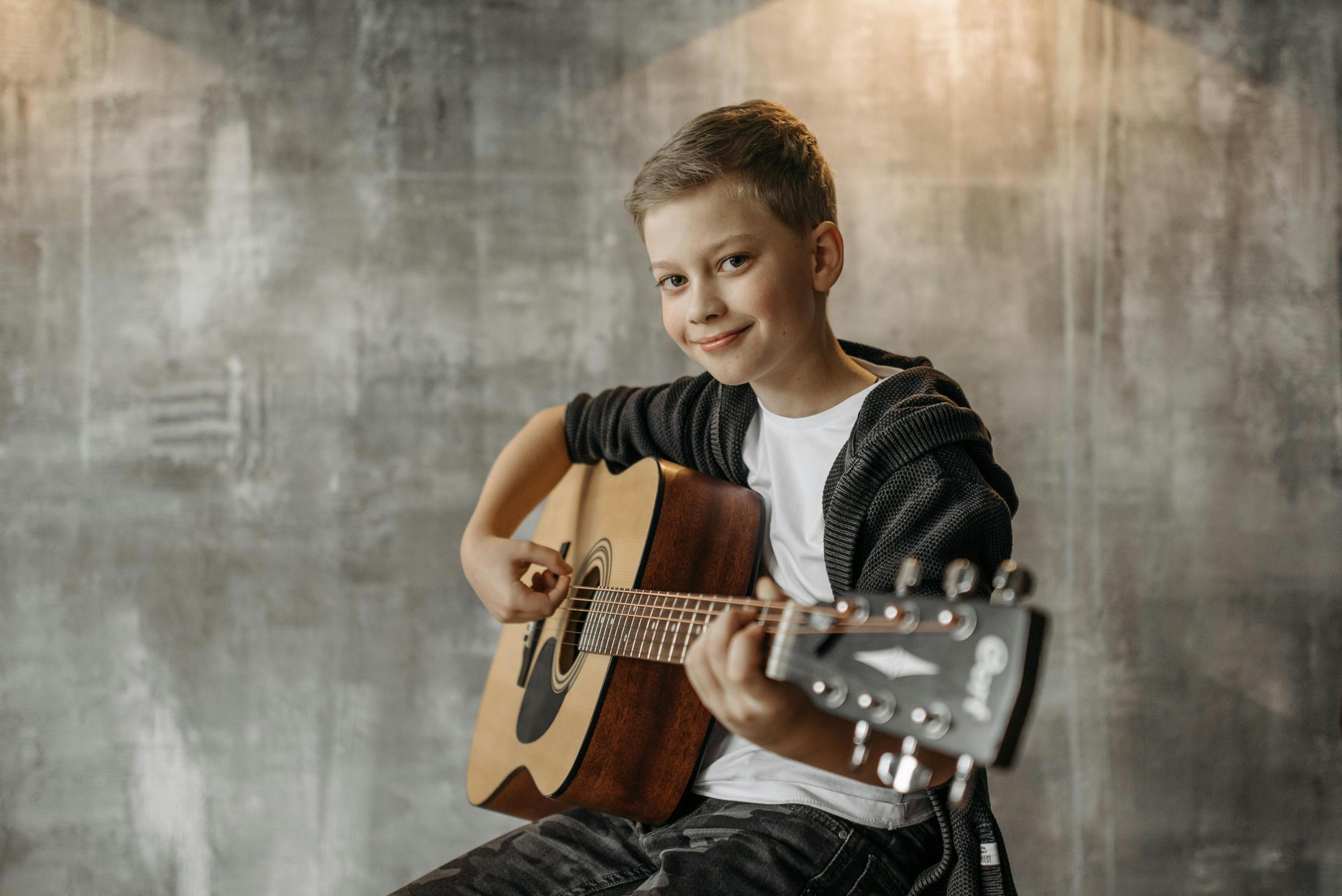 Jongen met akoestische gitaar glimlacht terwijl hij speelt.