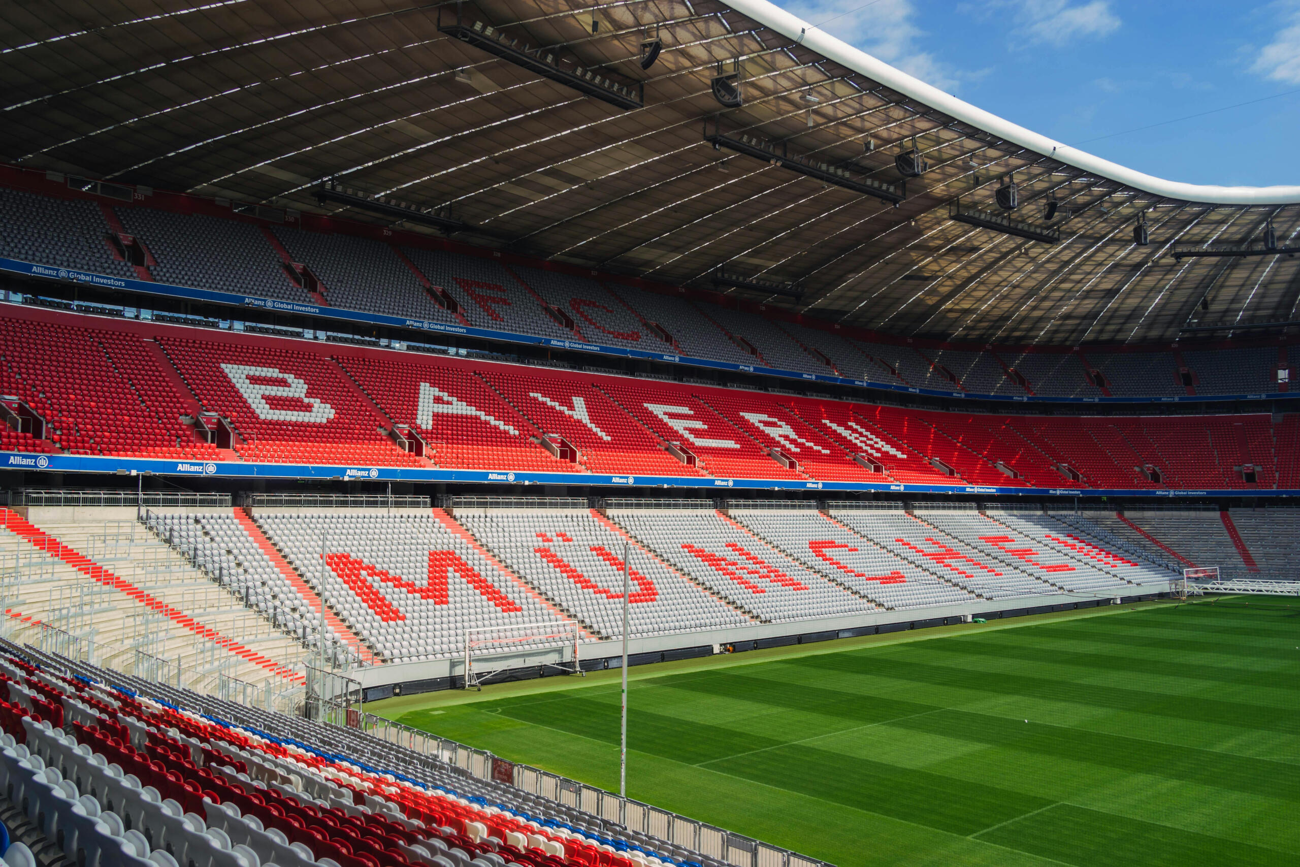 Een panoramisch beeld van de Allianz Arena in München, met lege tribunes in opvallend rood en wit.