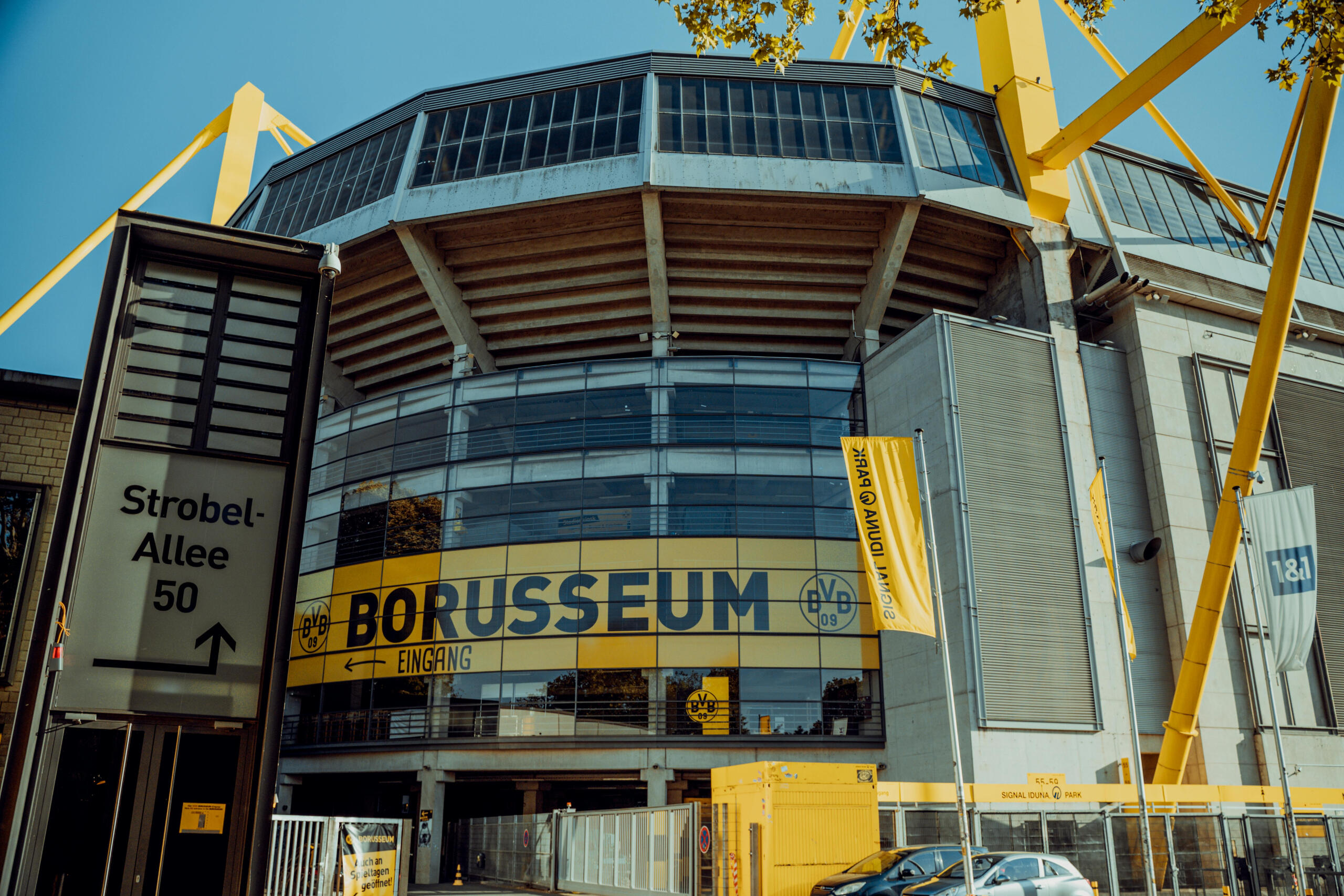 De ingang van Signal Iduna Park, met het Borusseum prominent in beeld, omgeven door gele accenten en een blauwe lucht.