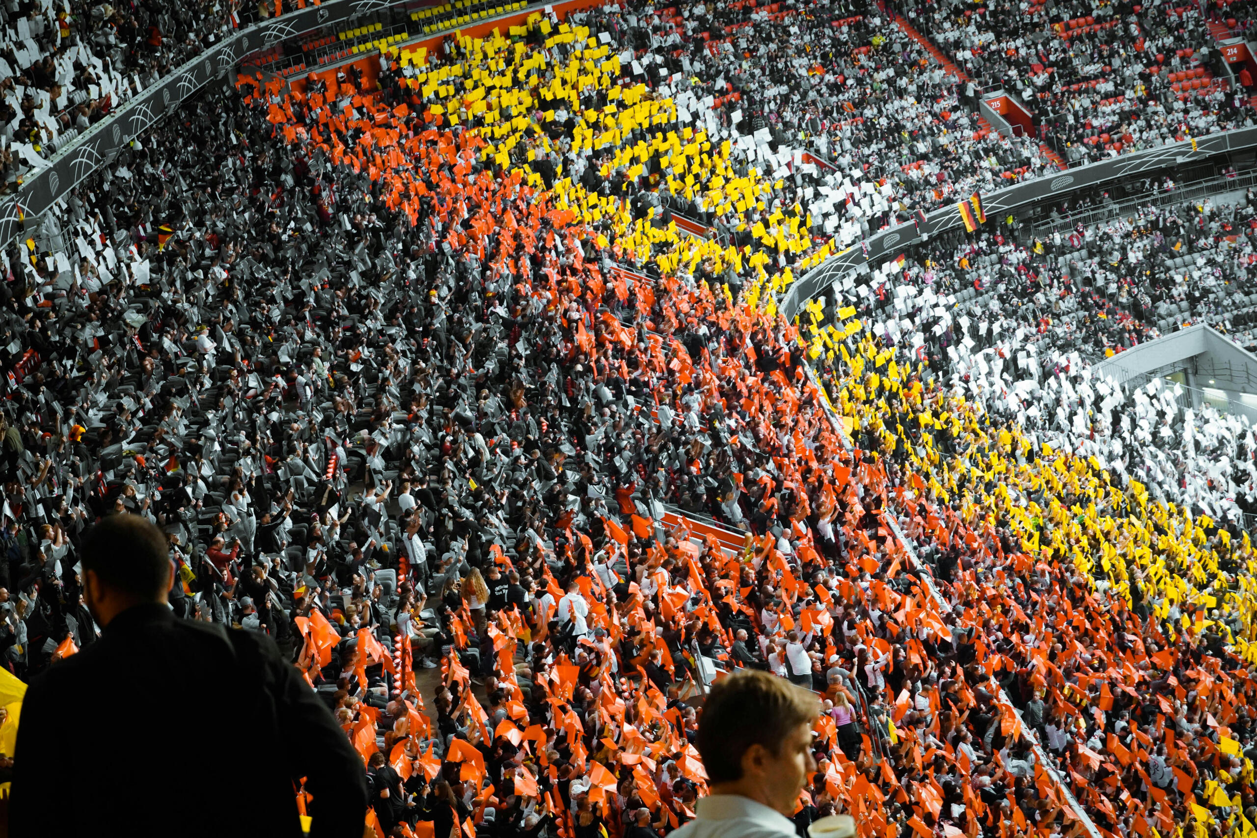 Een tribune vol enthousiaste supporters die kleurige borden omhooghouden in rood, geel en wit.