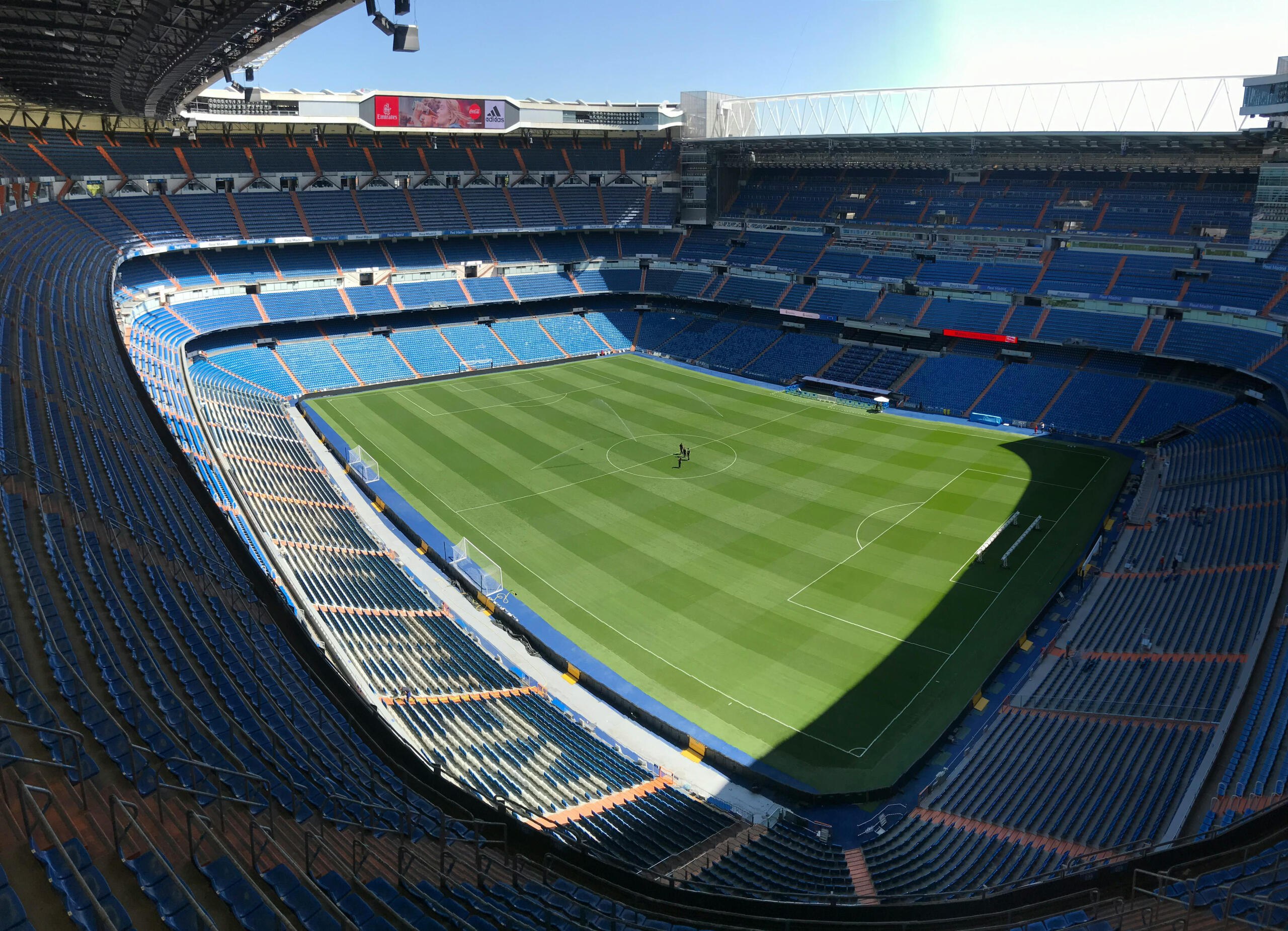 Santiago Bernabéu: leeg stadion van Real Madrid, blauwe stoelen, strak veld, zon en schaduw verdeeld.