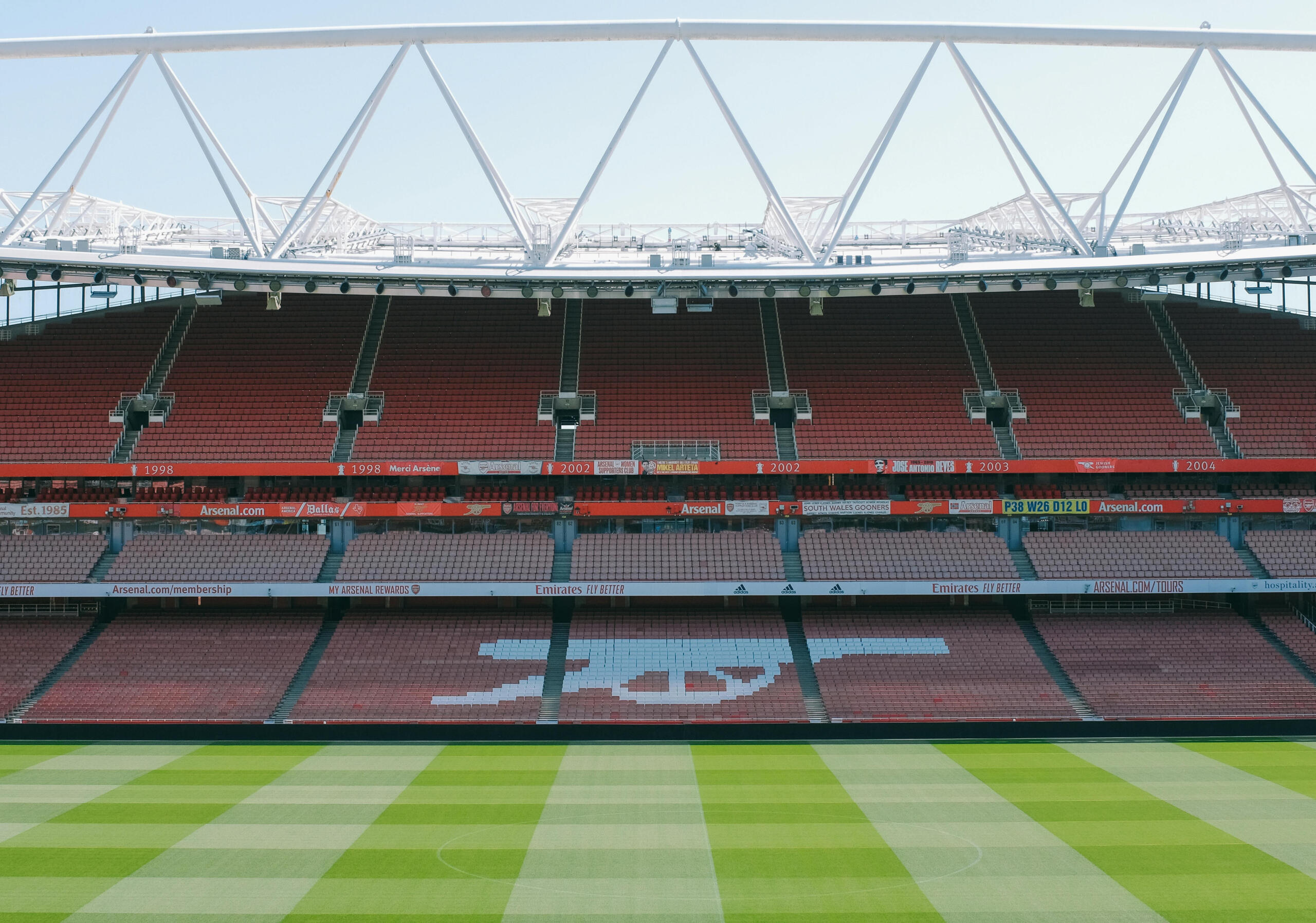 Een strak onderhouden grasveld en rode tribunes met het iconische Arsenal-kanonlogo.