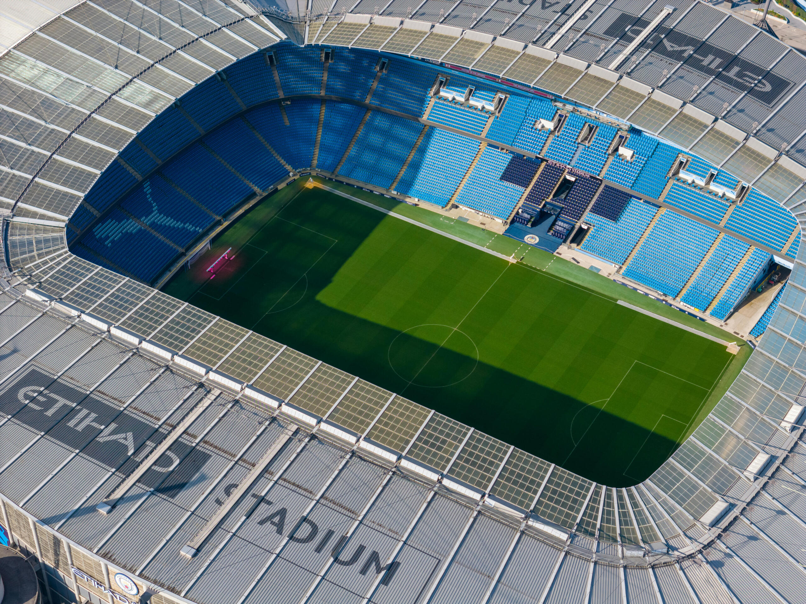 Een vogelperspectief van het modern Manchester City stadion met een helderblauwe tribune en perfect gemaaid gras.