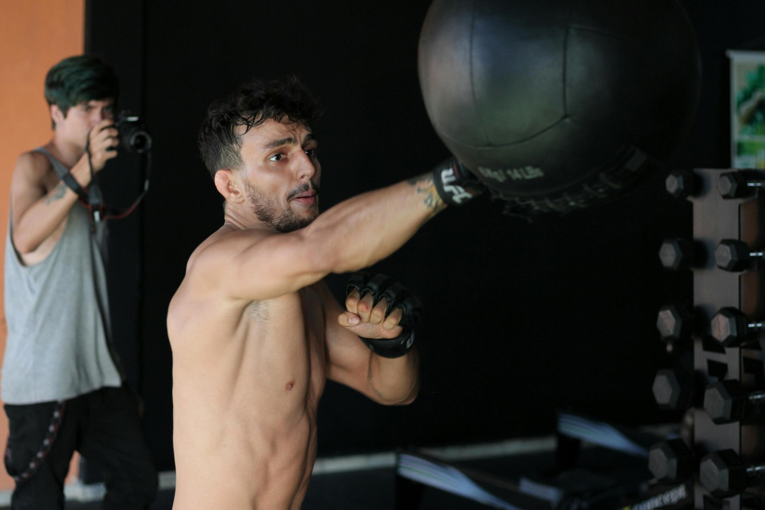 Een man traint met een medicine ball in een sportschool, terwijl een fotograaf zijn training vastlegt.