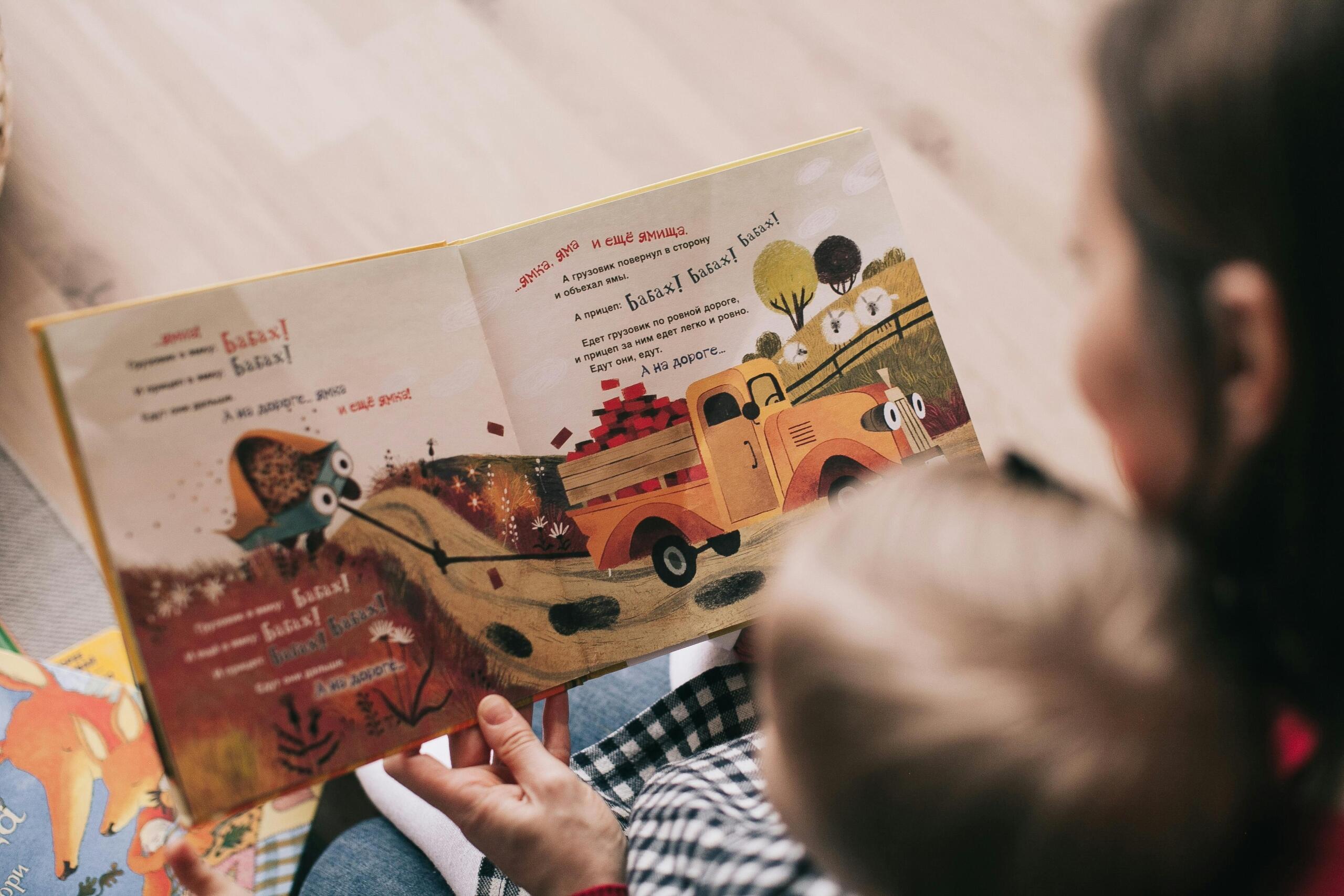Een persoon leest een kleurrijk geïllustreerd kinderboek voor aan een kind dat op schoot zit.