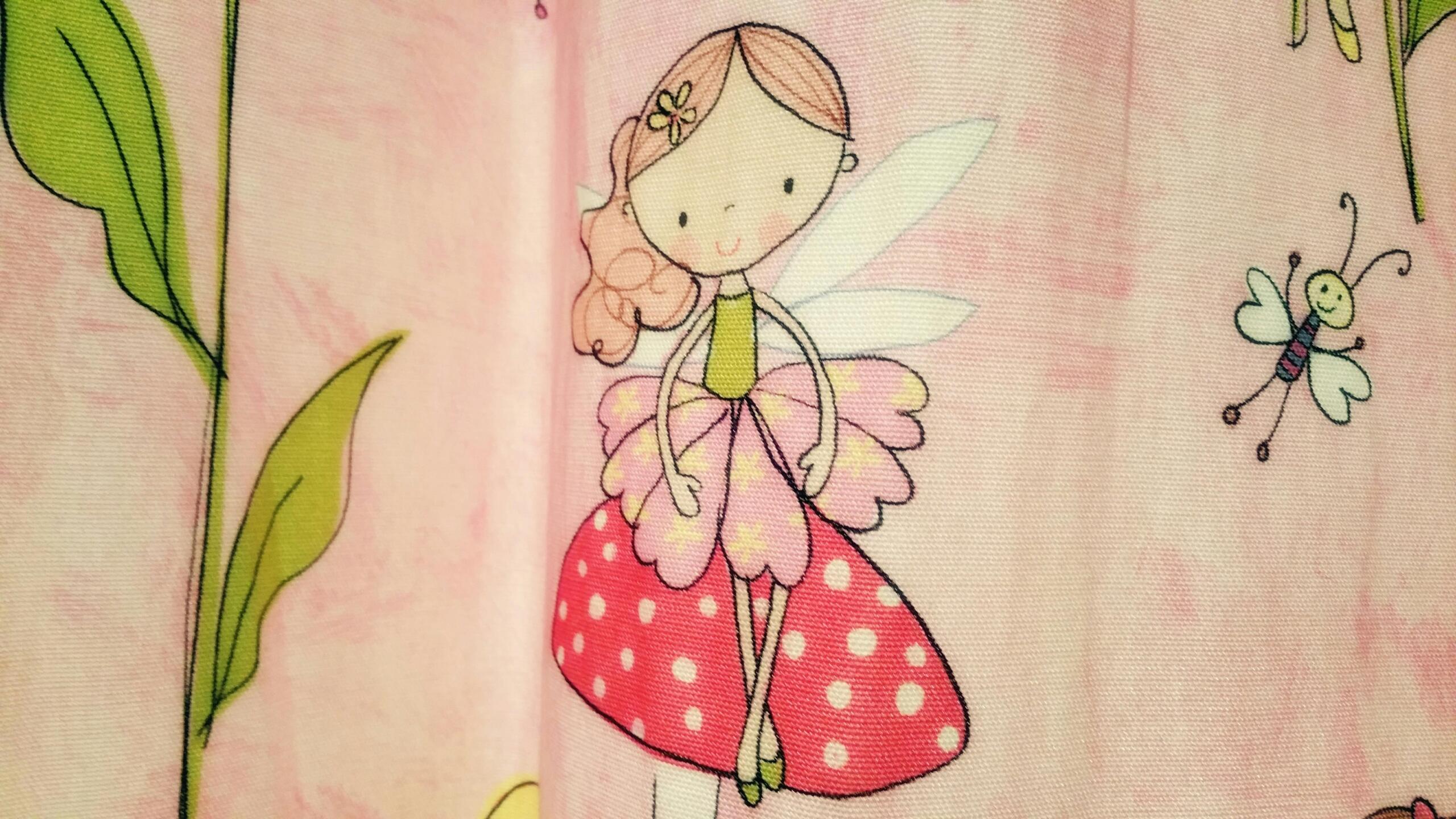 Een roze doek met een tekening van een glimlachende fee met vleugels en een stippenjurk, naast een vrolijke vlinder.