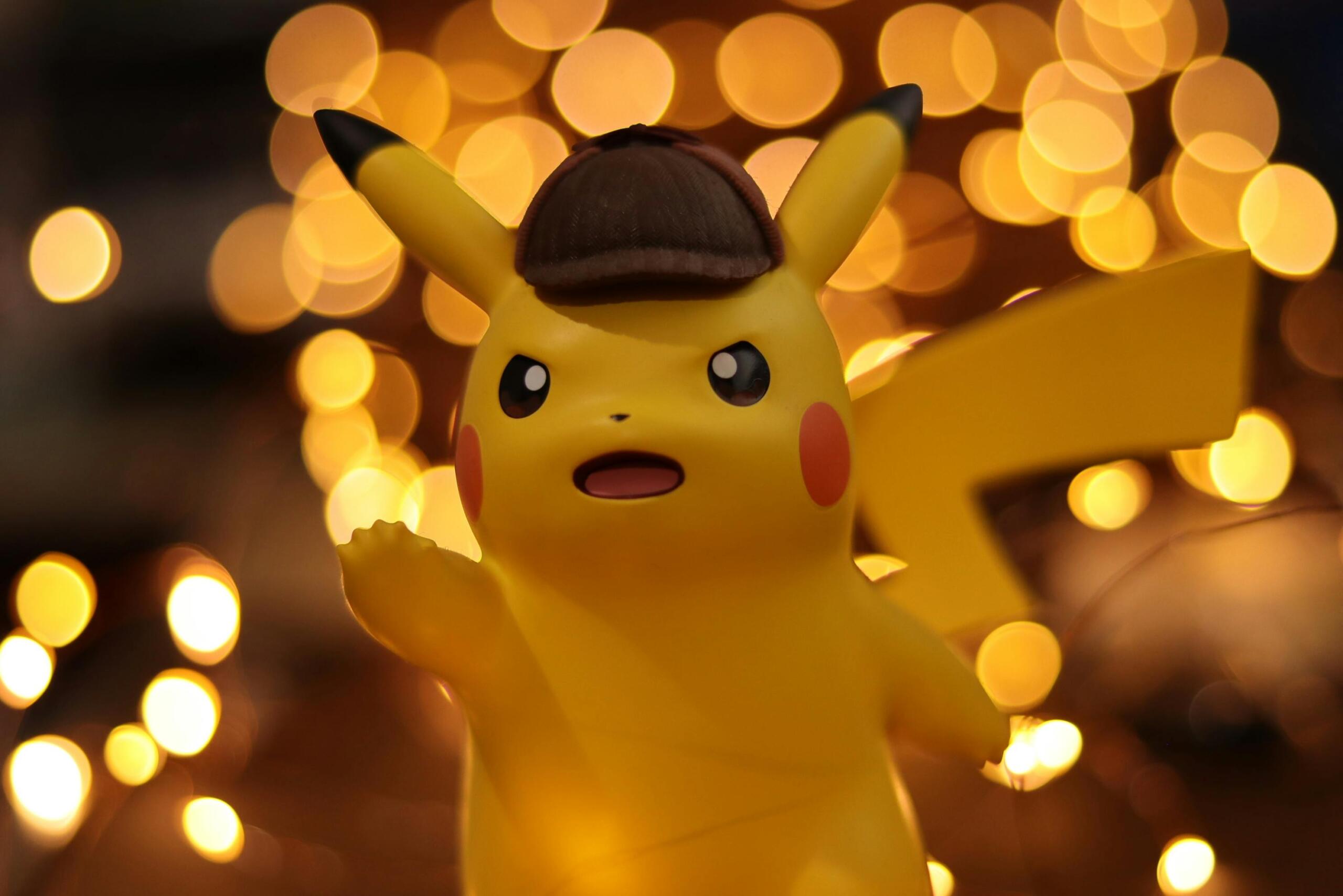 Een Pikachu-figuur met een detectivehoed op, met een achtergrond van warme, wazige lichtjes.
