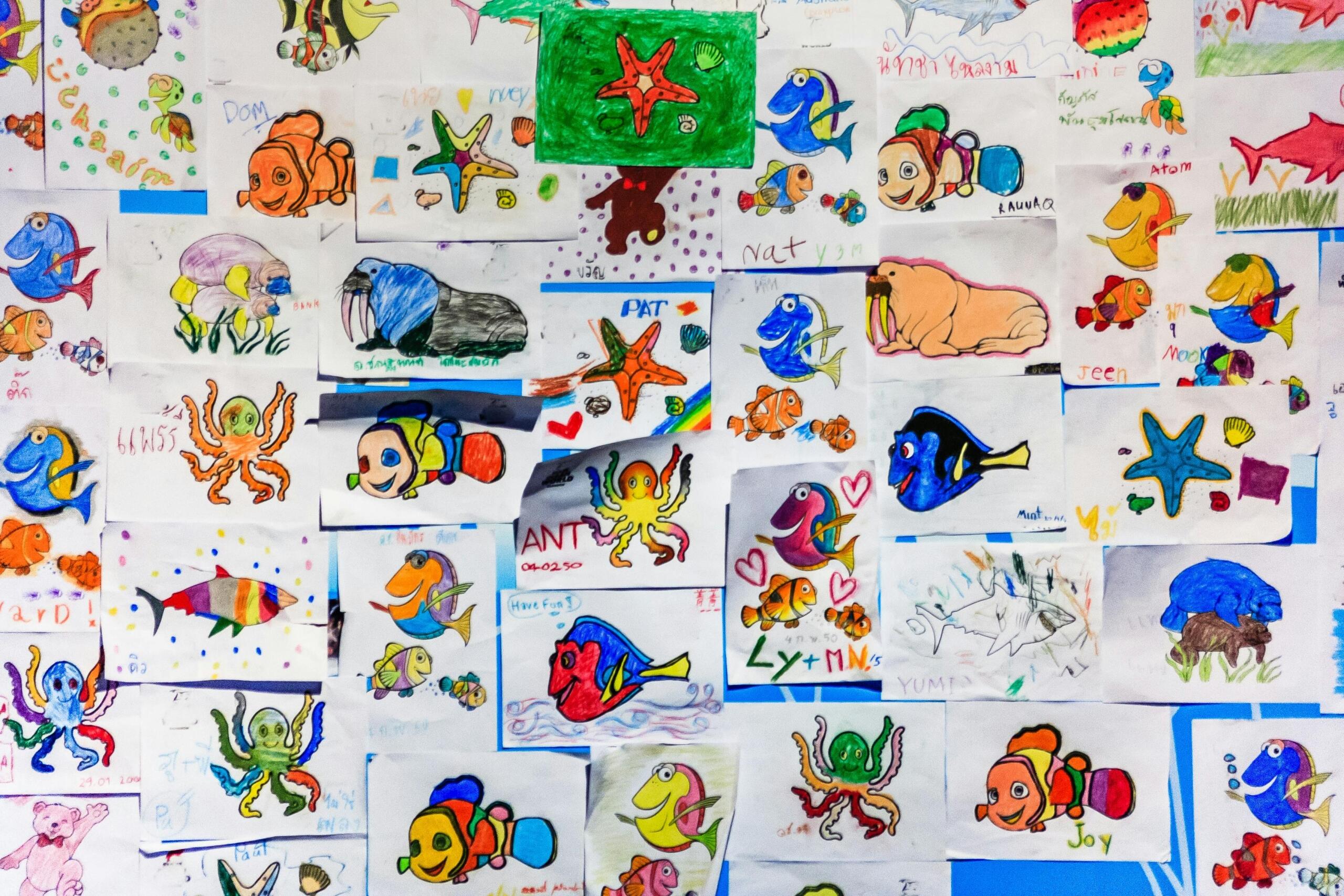 Een muur vol met kindertekeningen van zeedieren, waaronder vissen, octopussen en zeesterren, in verschillende kleuren en stijlen.