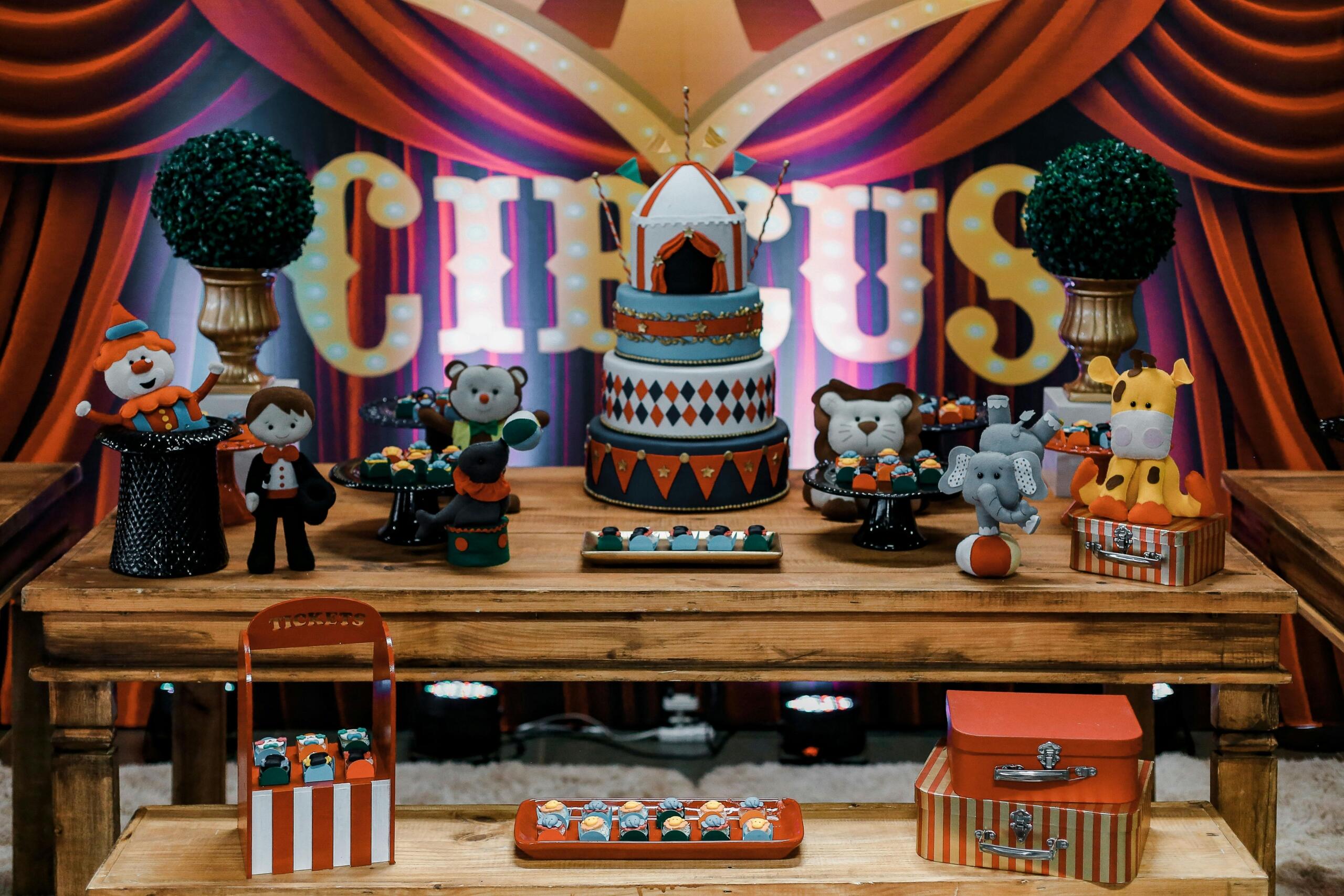 Een feestelijke circustaart met bijpassende decoraties zoals poppetjes, dierenfiguren en snoepjes op een houten tafel, met een kleurrijke achtergrond waarop "CIRCUS" staat.