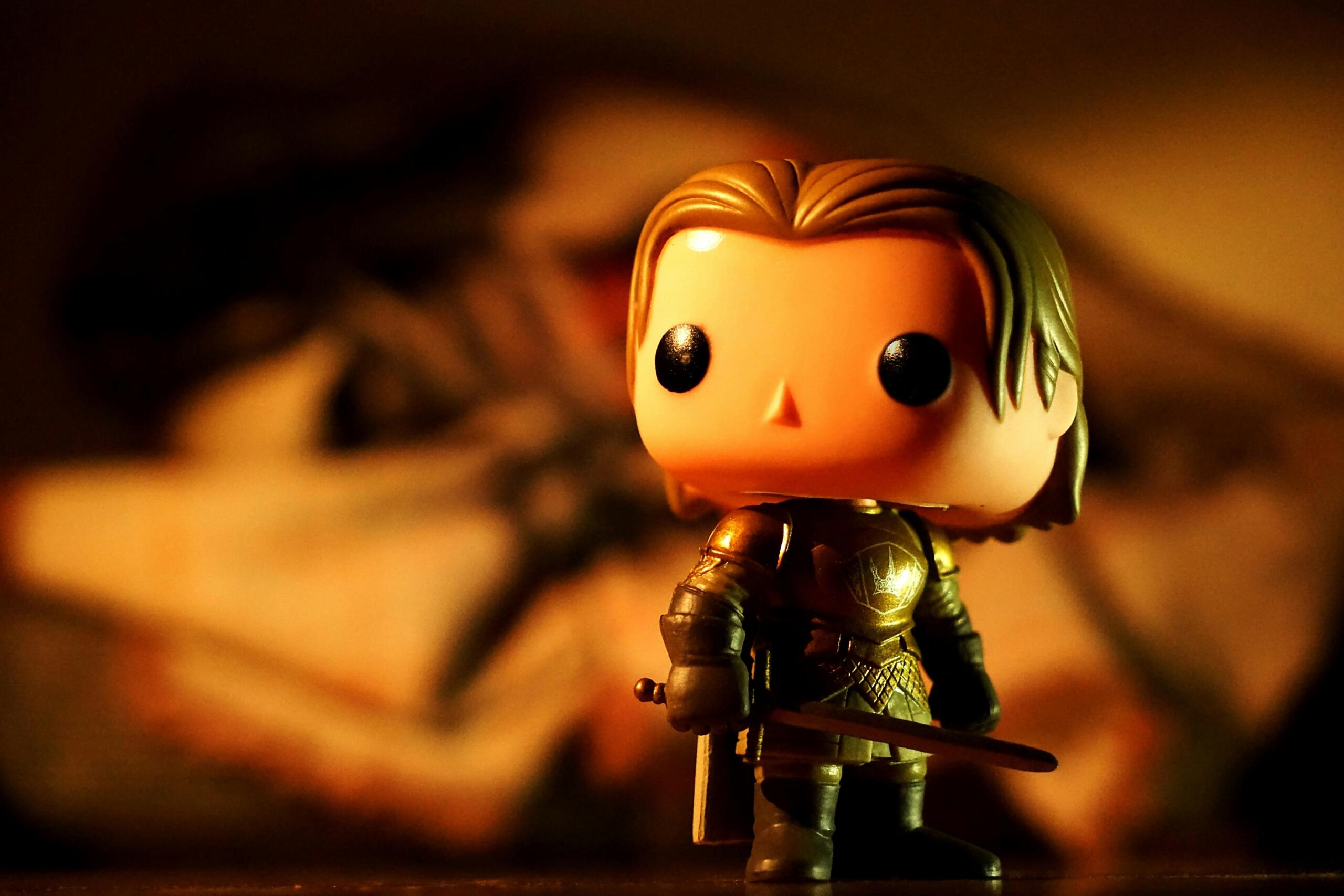 Een Funko Pop-figuur van een ridder in gouden harnas met een zwaard, sfeervol verlicht met een warme achtergrond.