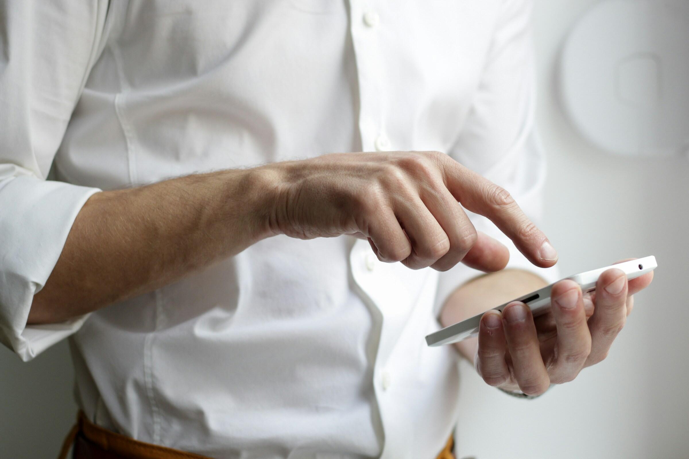 Persoon in wit overhemd met iPhone in hand wijst iets aan