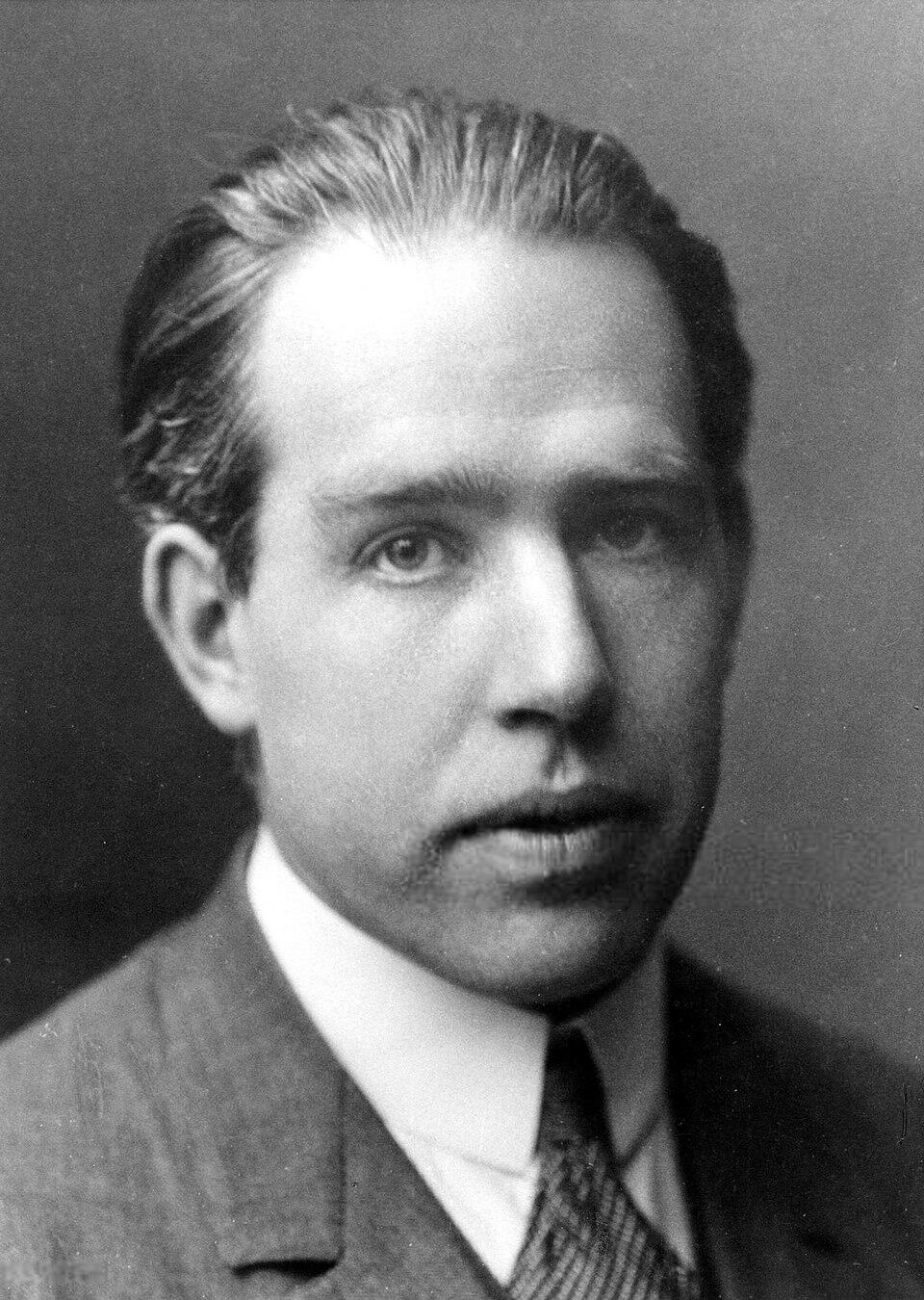 Zwart-witportret van Niels Bohr in een pak, zittend en kijkend naar de camera.