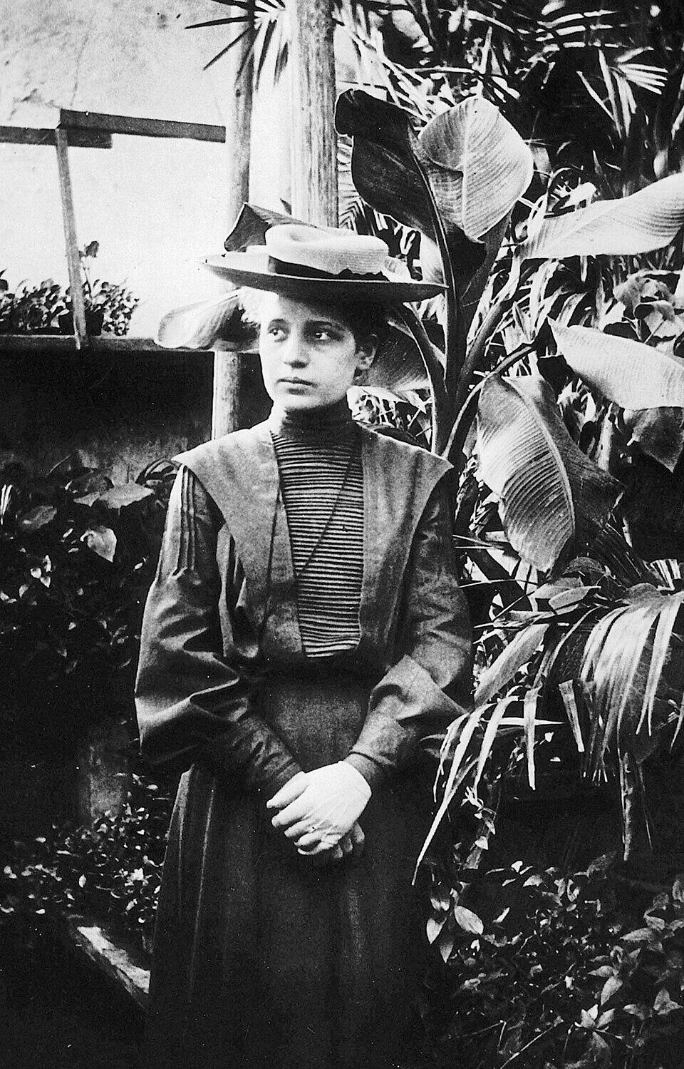 Zwart-witfoto van Lise Meitner zittend aan een bureau in een laboratorium, kijkend naar de camera.