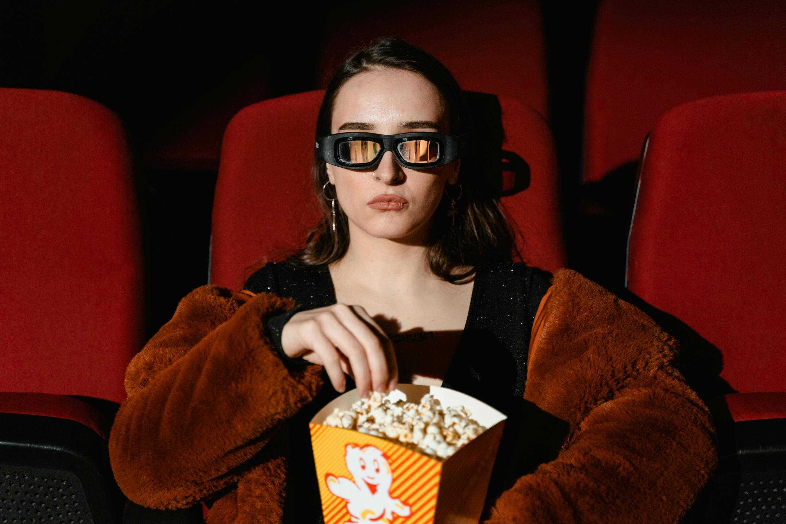 Vrouw met 3D-bril zit in de bioscoop met popcorn op schoot.