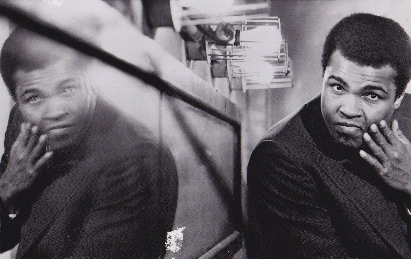 Zwart-wit persfoto van Muhammad Ali in 1971. Hij kijkt zelfverzekerd naar de camera terwijl hij zijn bokshandschoenen omhoog houdt in een klassieke vechthouding.