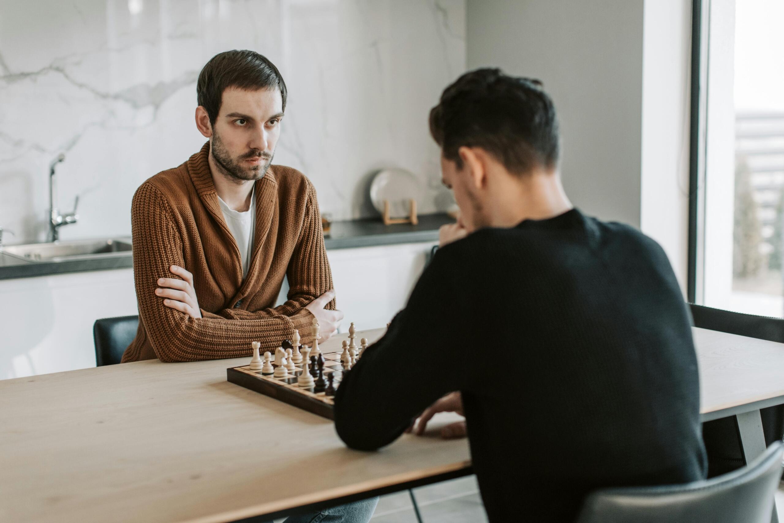 Twee mannen zitten geconcentreerd tegenover elkaar aan tafel met een schaakbord tussen hen in.