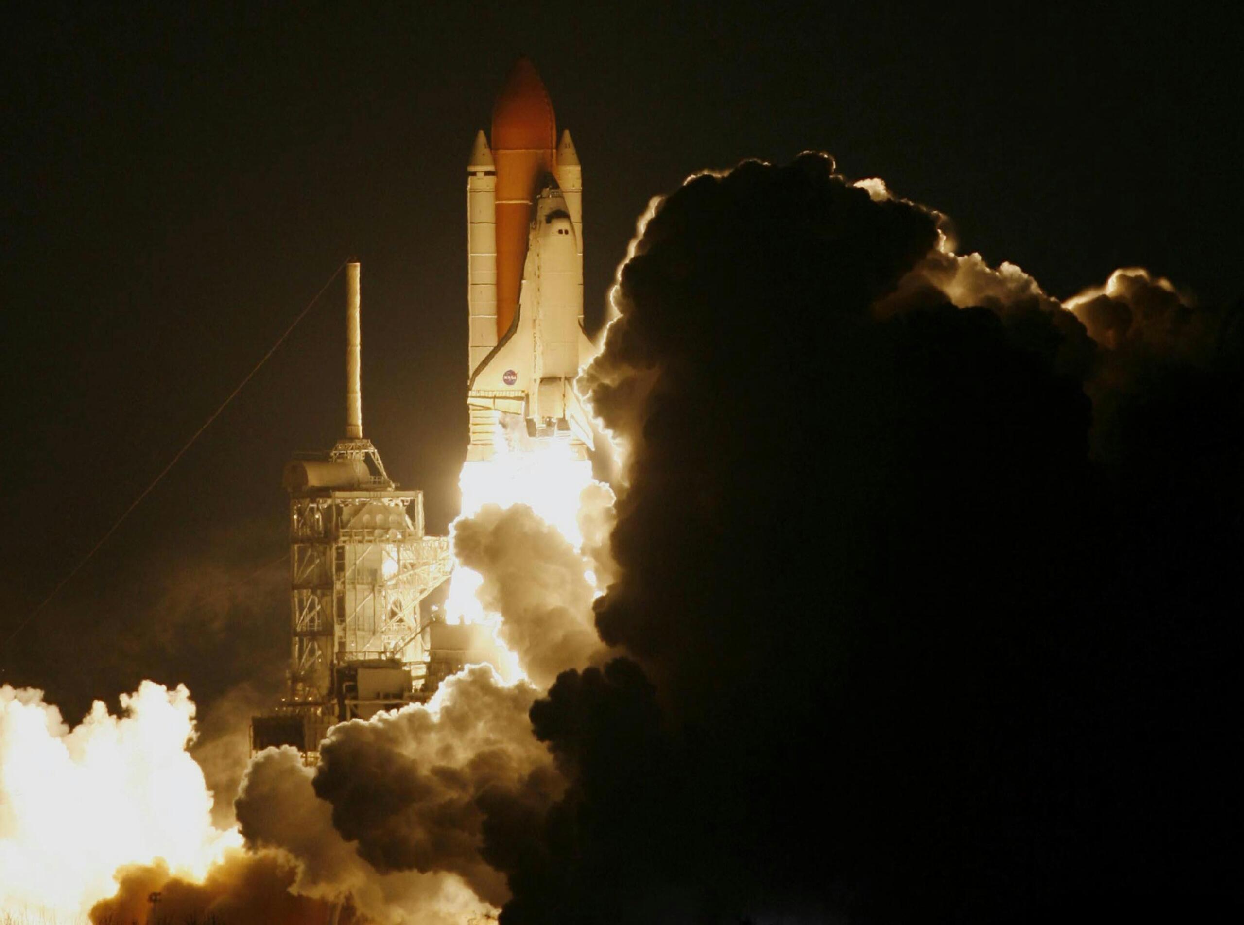 Nachtelijke lancering van een spaceshuttle, fel verlicht met dikke rookwolken.