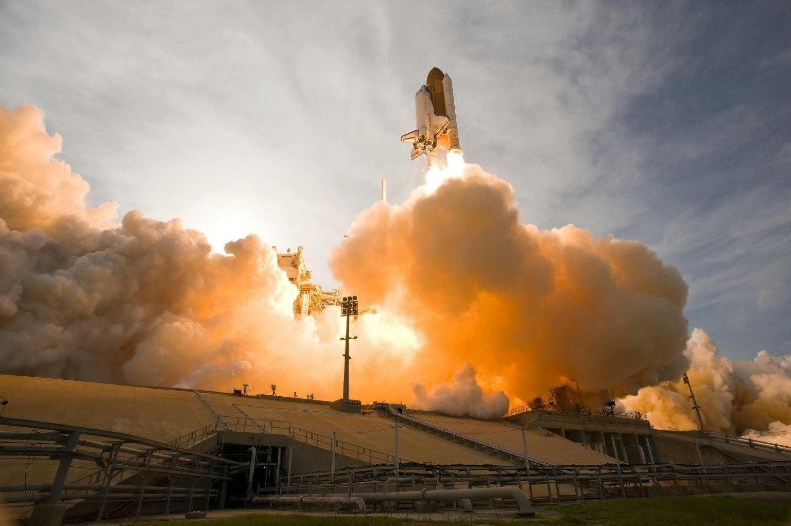 Lancering van een spaceshuttle vanaf lanceerplatform met rookwolken.