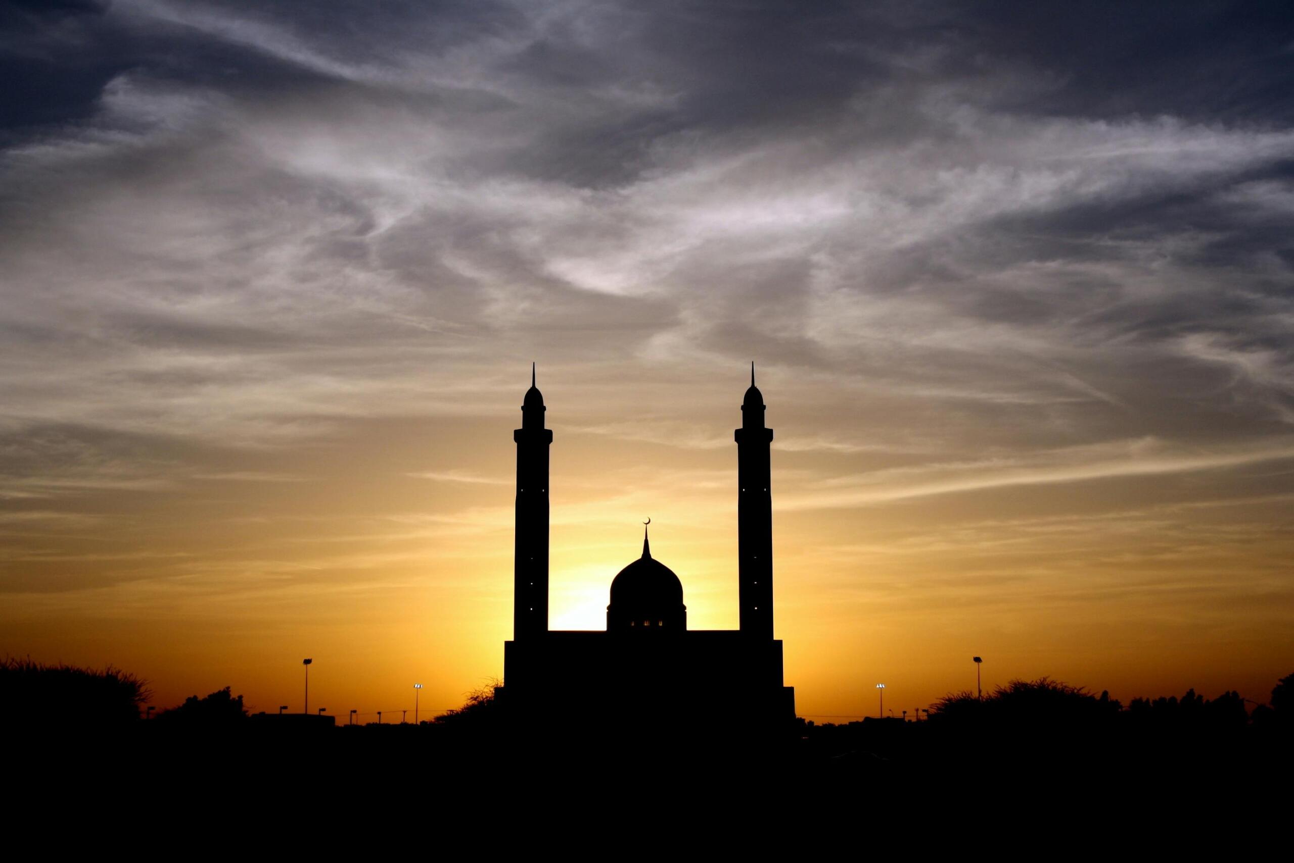 Silhouet van een moskee met twee minaretten tegen een ondergaande zon.