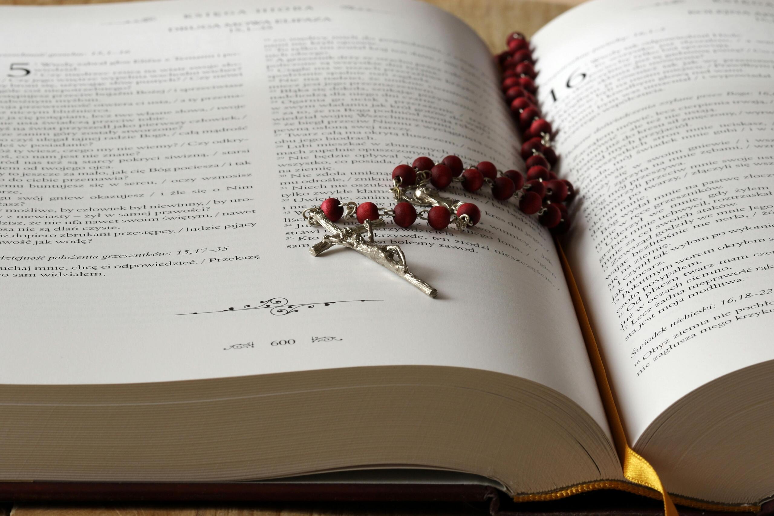 Een rozenkrans met crucifix ligt opengeslagen op een religieus boek.