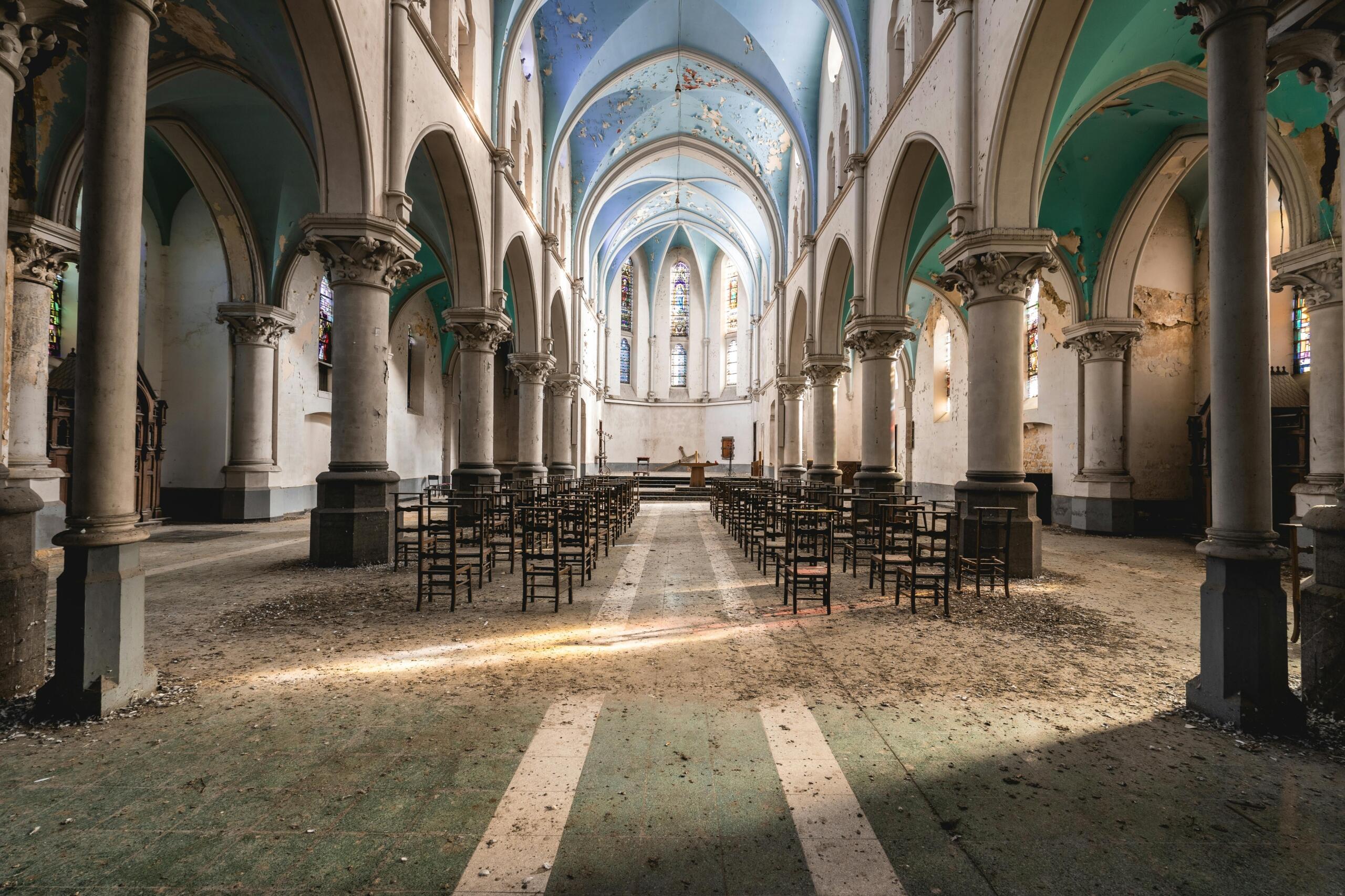 Verlaten kerk met vervallen interieur, waarbij het licht door de gebroken ramen naar binnen valt.