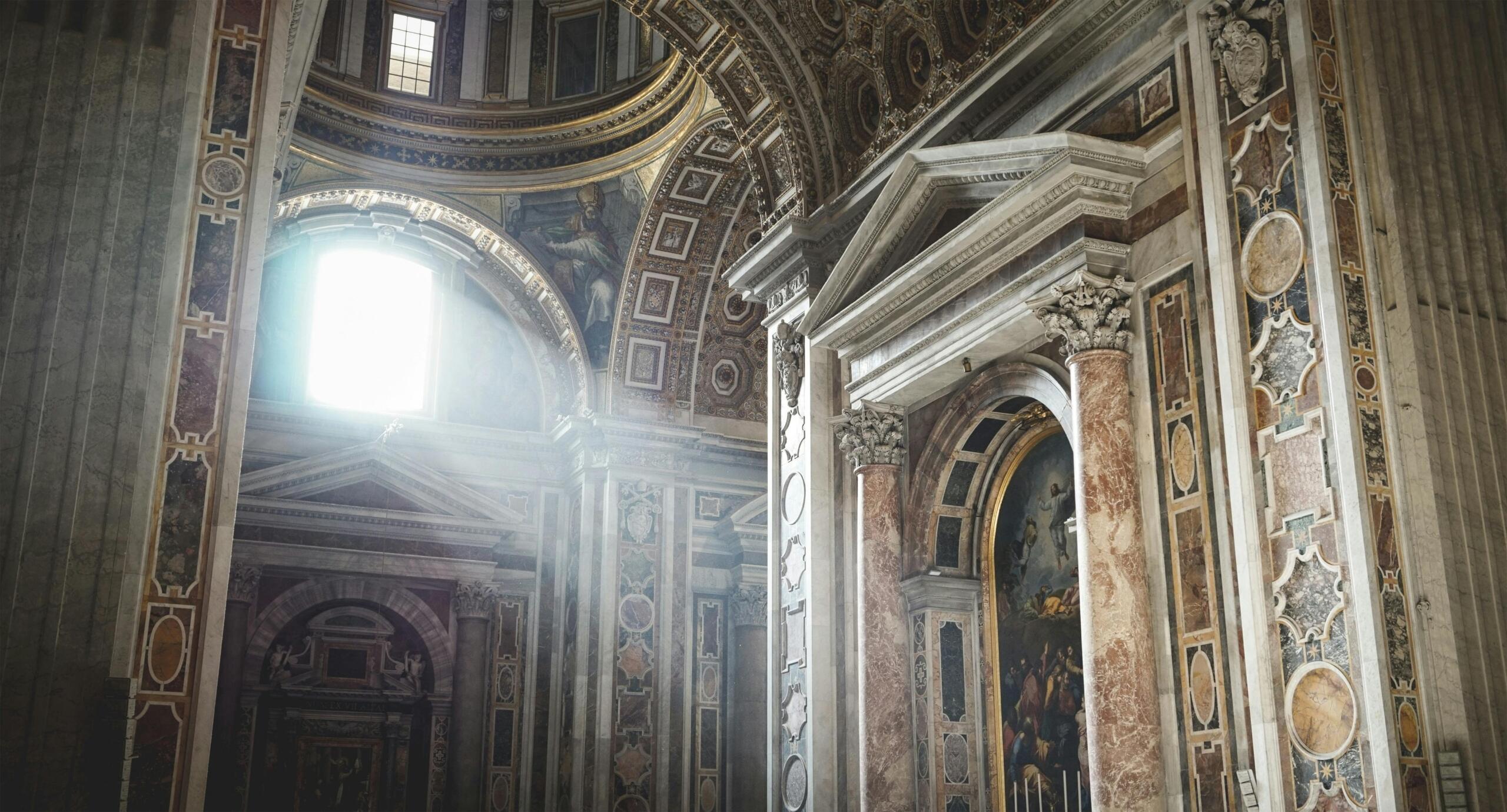 Binnenzijde van een rijk versierde basiliek, waar zonlicht een straal werpt op marmeren zuilen en fresco’s.