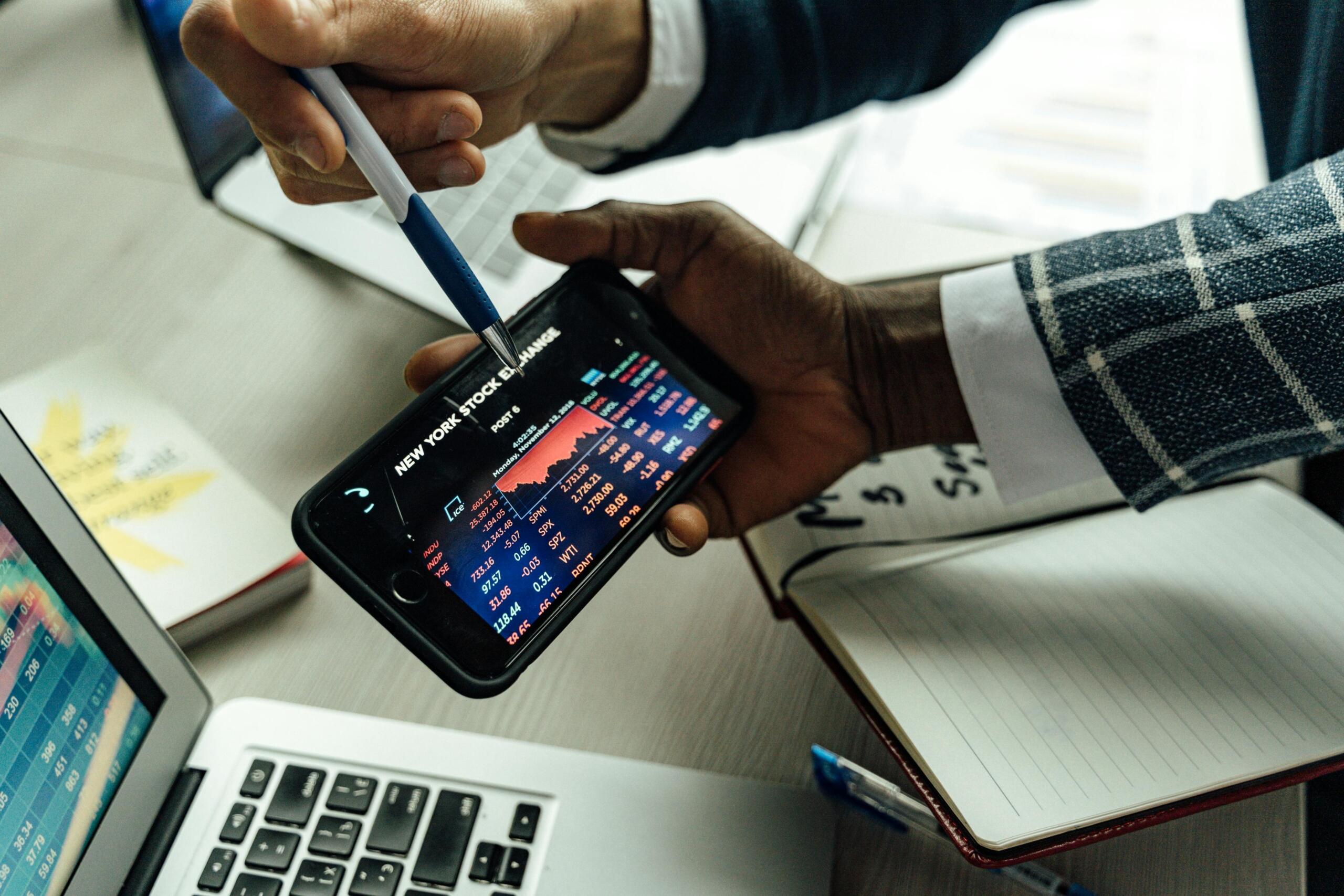 Twee zakenmannen analyseren beursgegevens op een smartphone.