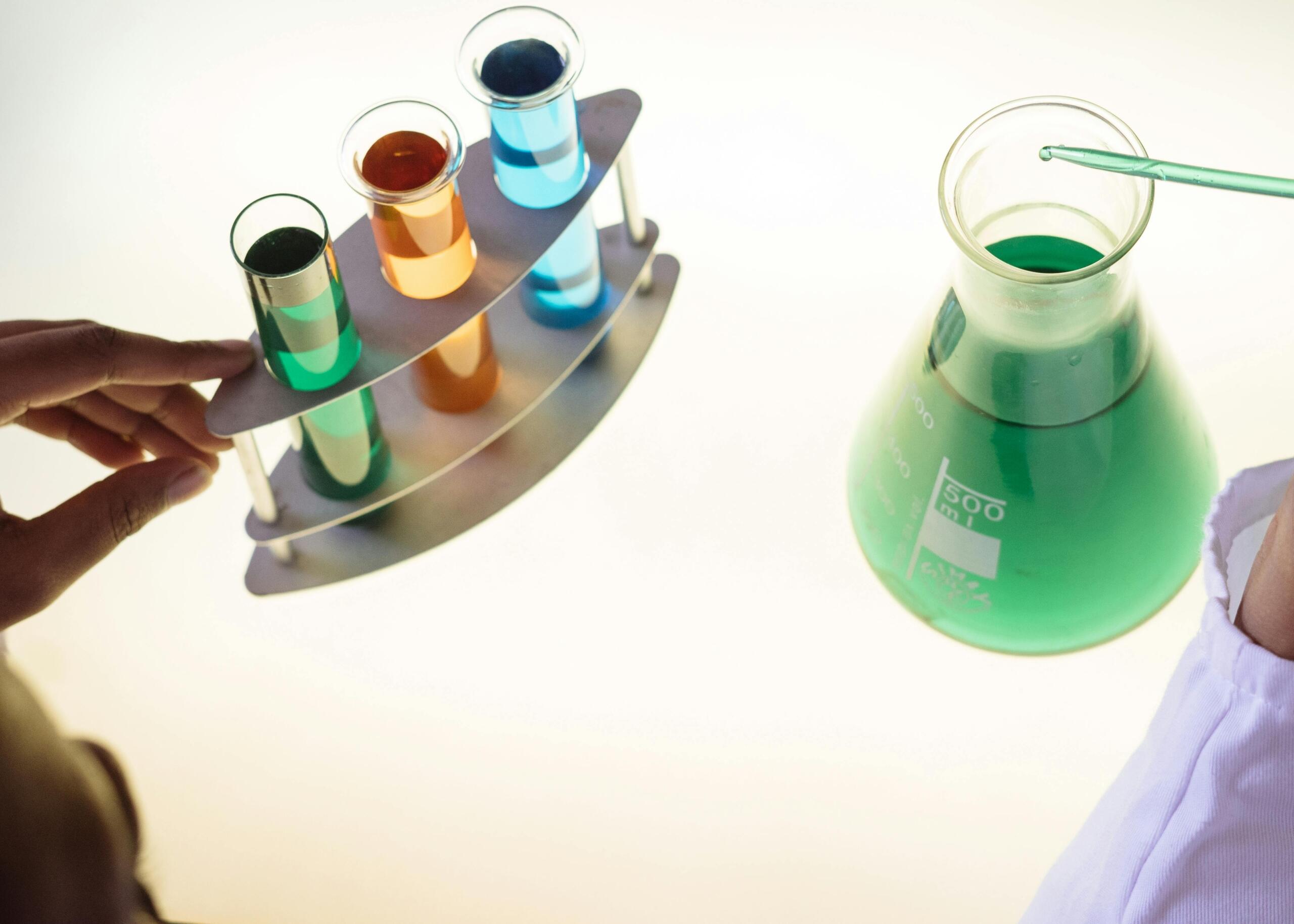 Reageerbuizen en erlenmeyer met gekleurde vloeistoffen en pipet.