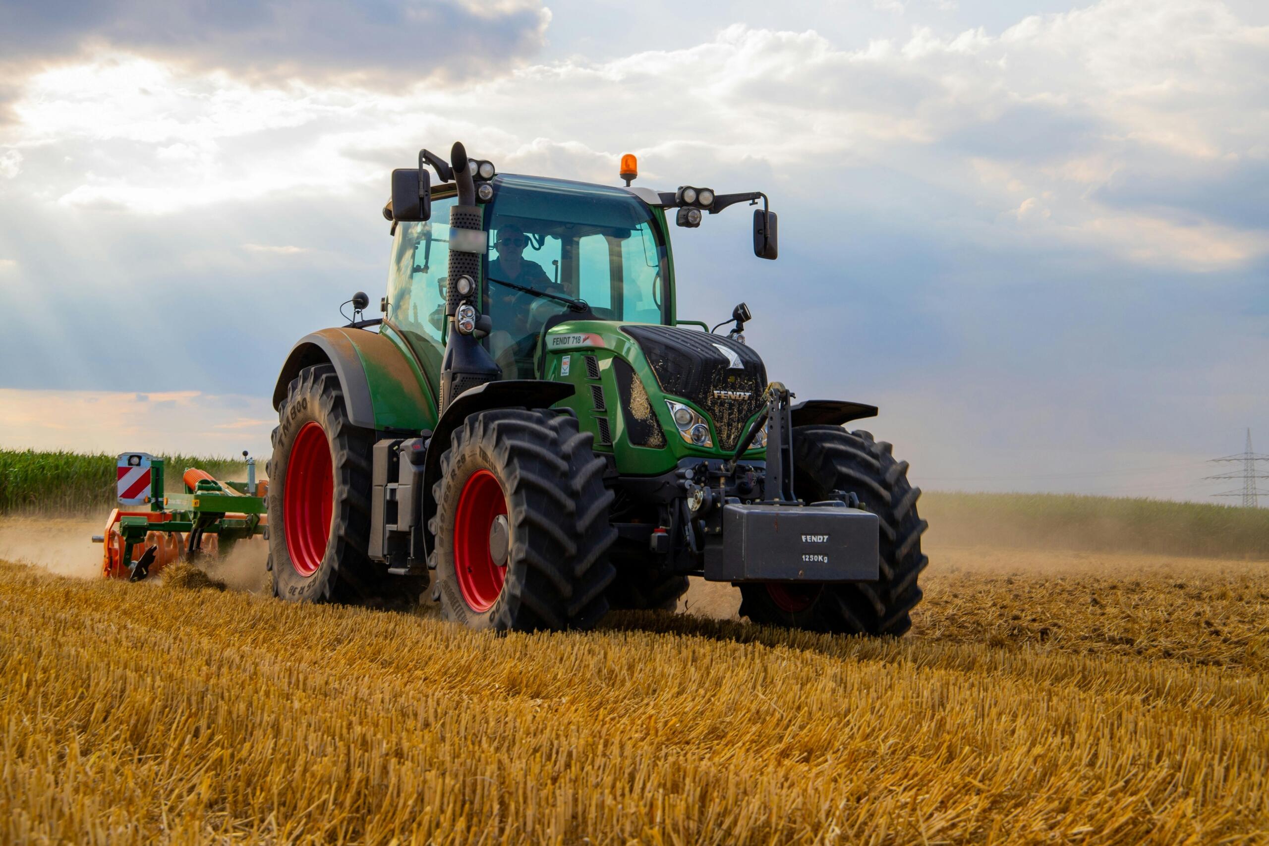 Een groene tractor die door een geel veld rijdt.